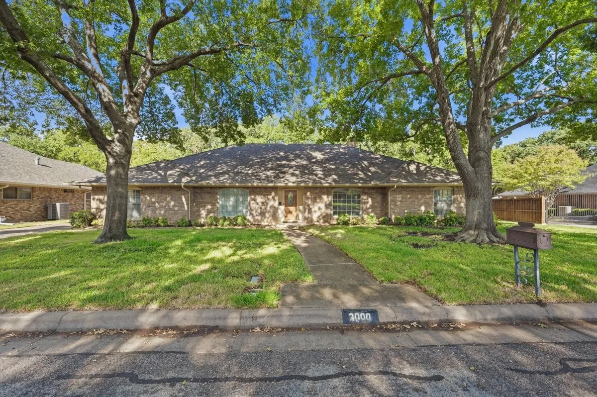 Brick-clad exterior with a prominent front door and multiple windows, framed by mature trees