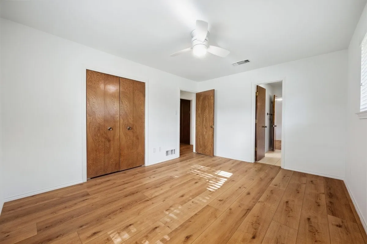 Wood-finish flooring, white walls, ceiling fan with integrated lighting, and multiple wood-paneled doors