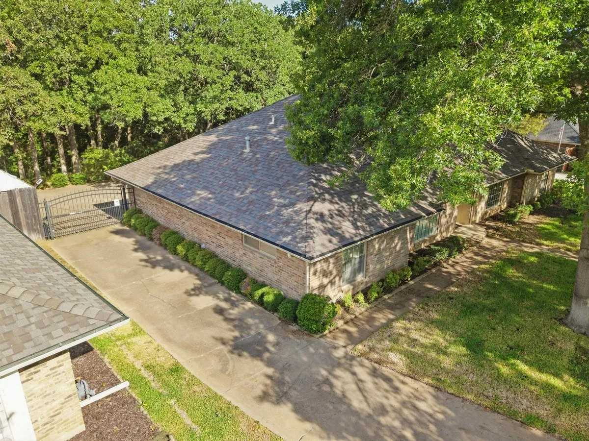 Brick exterior residence with a shingle roof, established landscaping, and a gated driveway