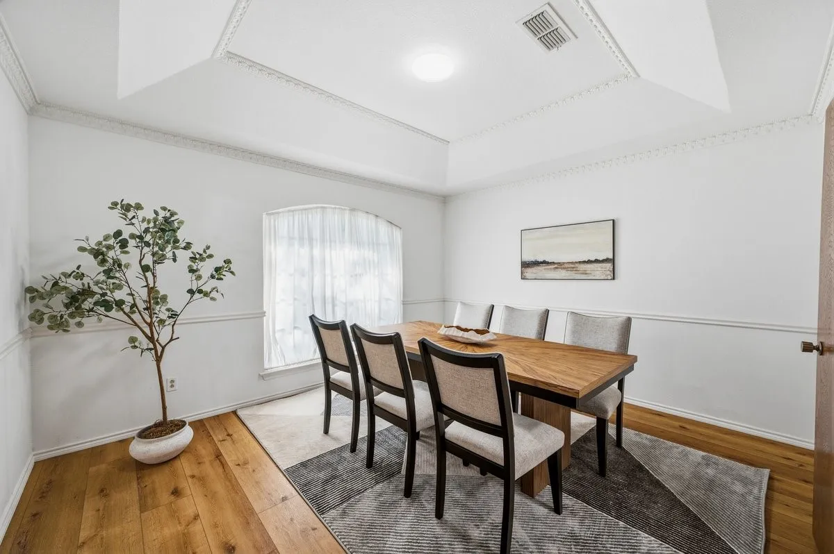 Tray ceiling with decorative molding, wood-finish flooring, white wainscoting, and a bay window