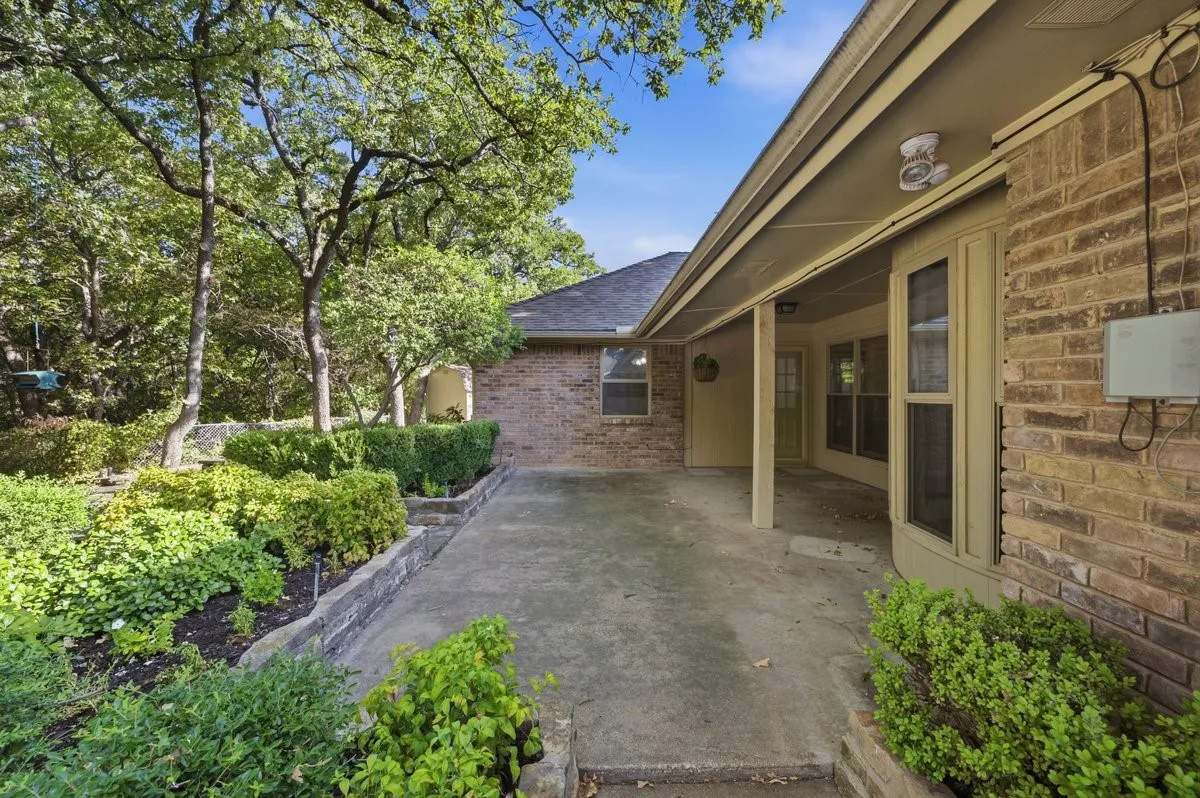 Brick exterior with covered patio, concrete hardscaping, multiple windows, and extensive landscaping