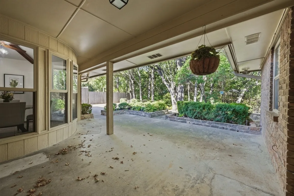 Covered patio with a concrete surface, supported by columns, featuring a curved bay window section and brick exterior