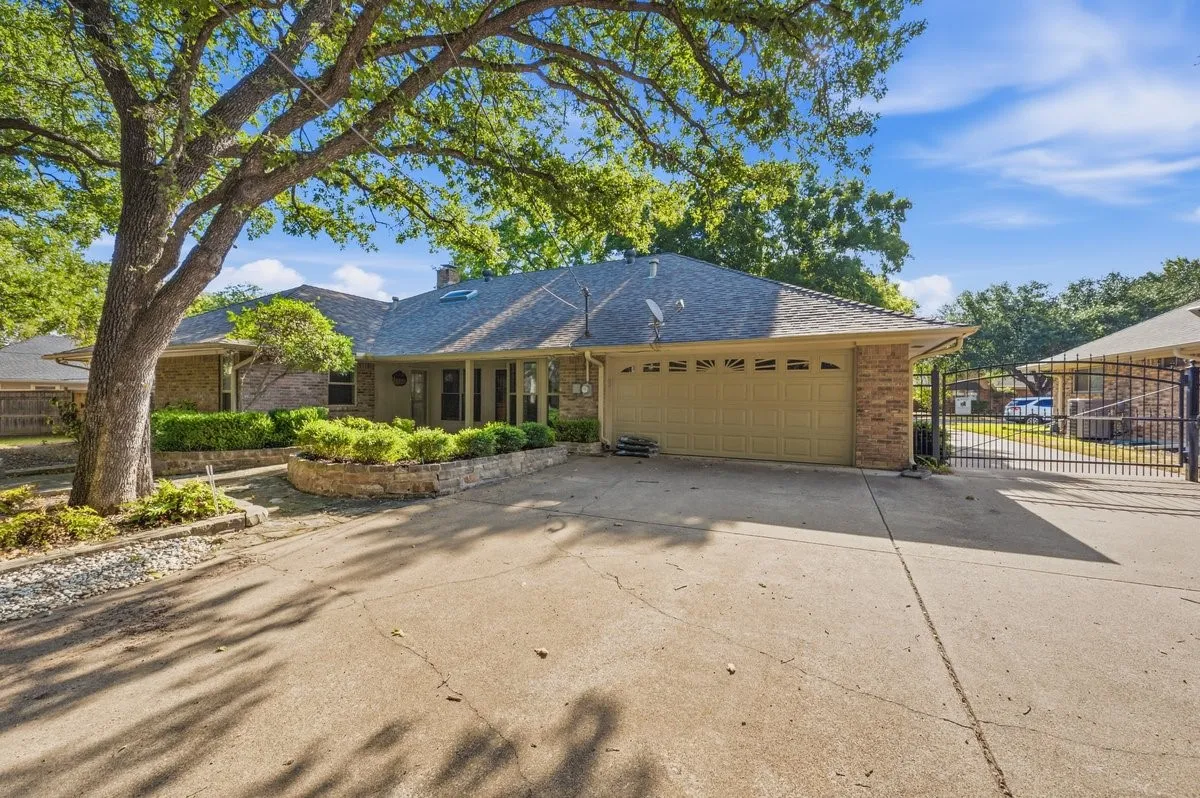 Brick exterior with an attached two-car garage, concrete driveway, and mature landscaping