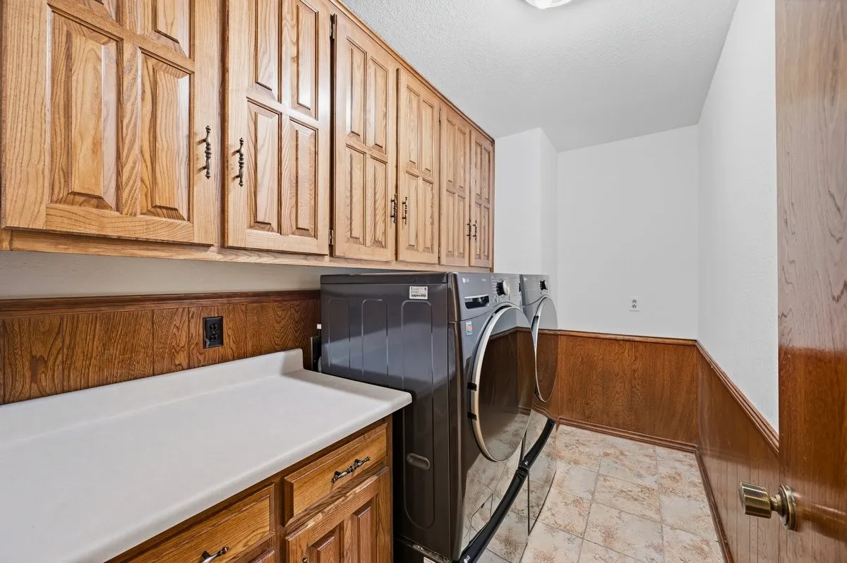 Wood-paneled laundry room with extensive cabinetry, a built-in countertop, and tile flooring