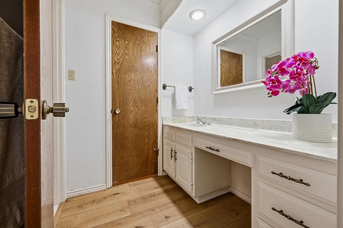 Wood-finish flooring, white vanity cabinetry with decorative hardware, light-toned countertop with integrated sink, and recessed lighting