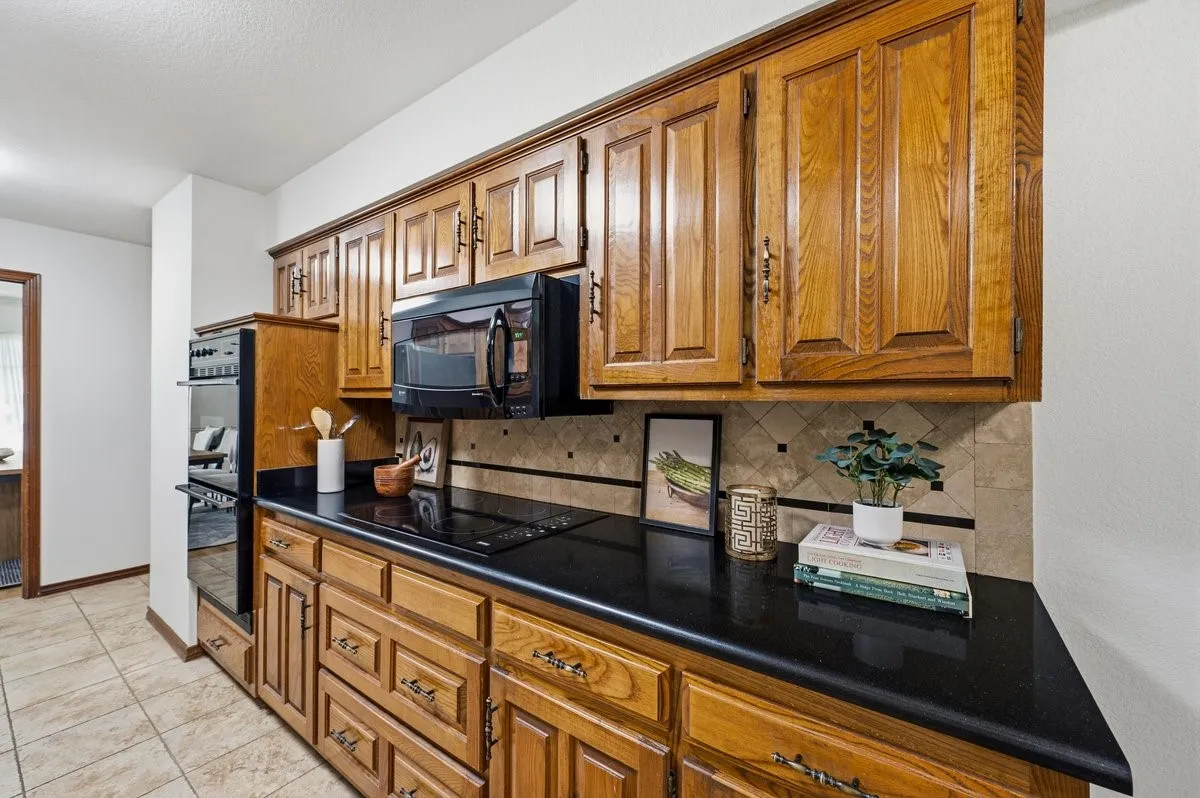 Kitchen featuring wood cabinetry, black countertops, tiled backsplash, built-in double oven, and stovetop