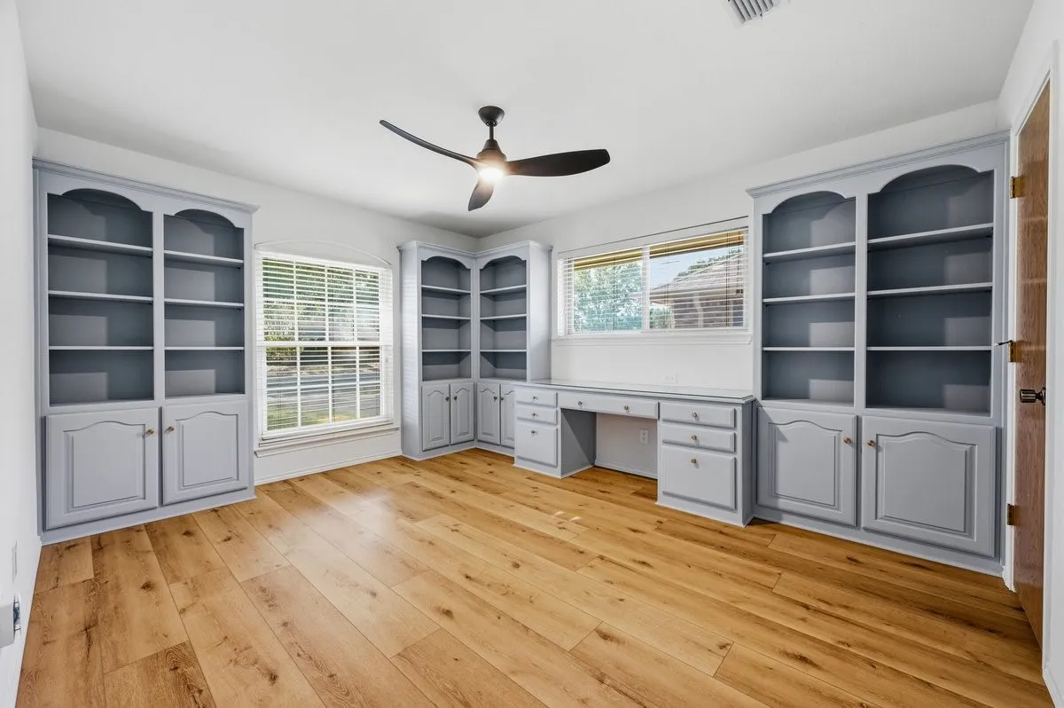 Wood-finish flooring with built-in cabinetry, a built-in desk, and multiple windows with blinds