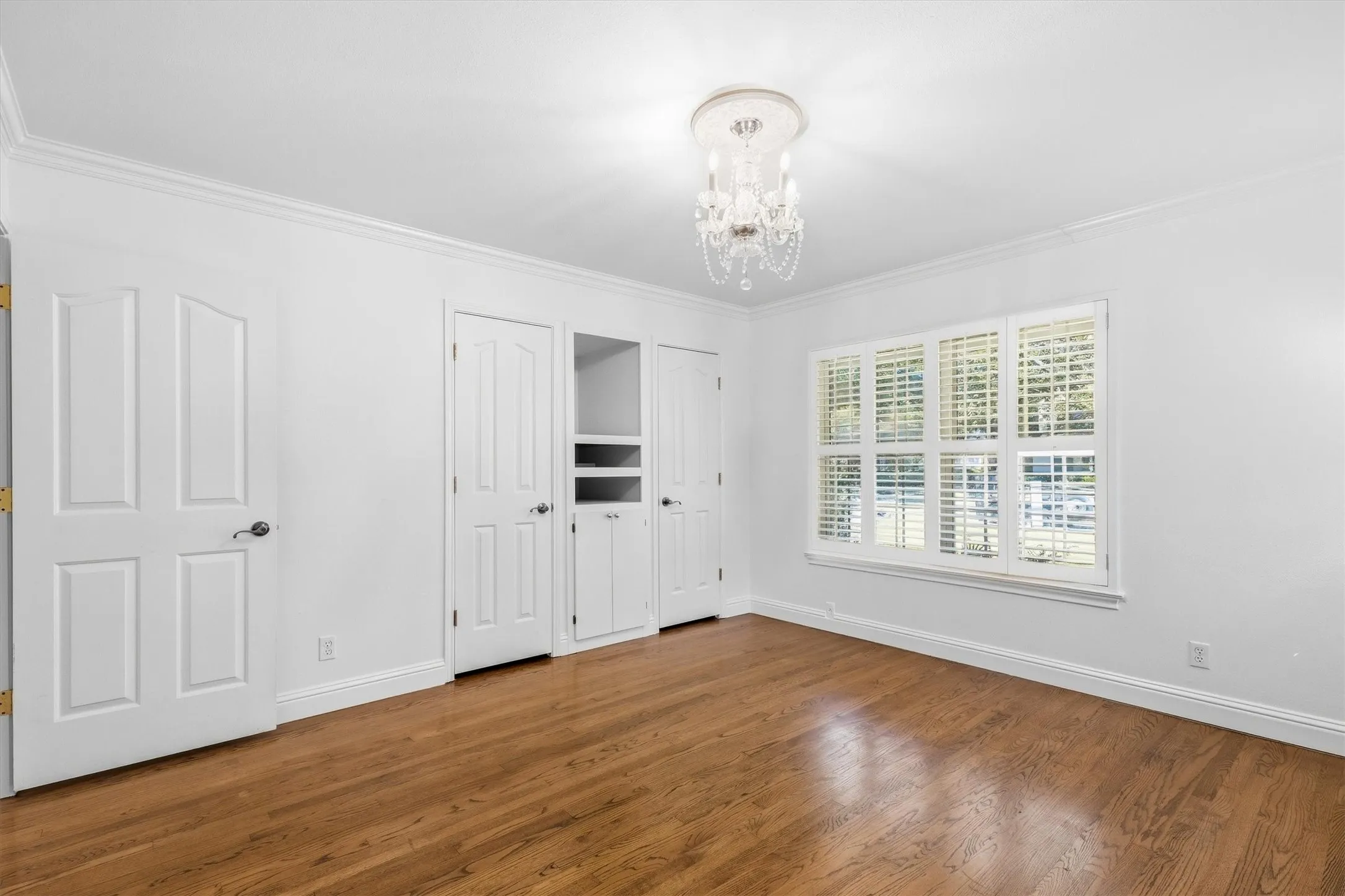 Hardwood flooring, crown molding, built-in storage, window with plantation shutters, and a chandelier lighting fixture