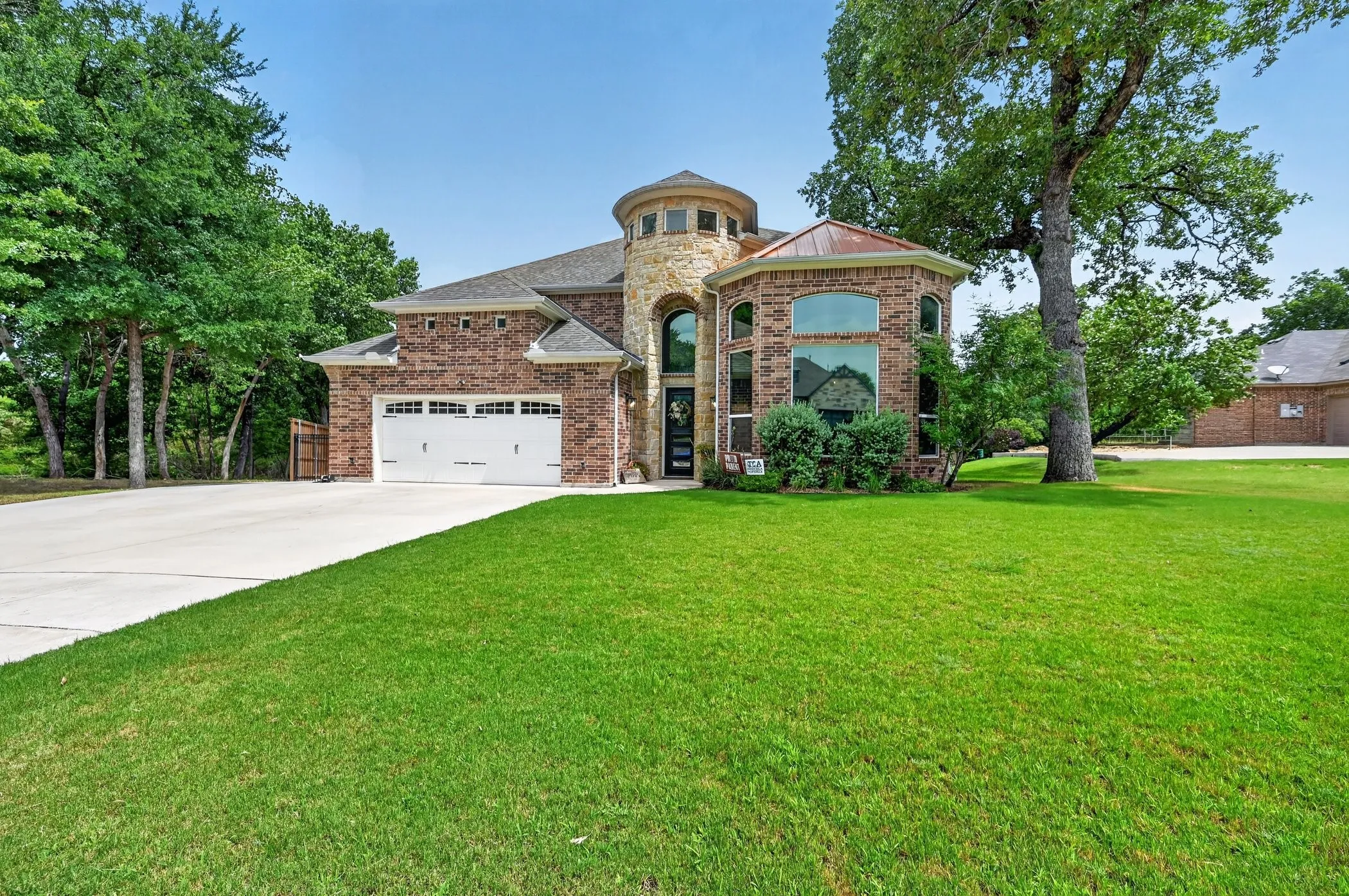 Brick exterior with a stone turret, multiple arched windows, an attached two-car garage, and a concrete driveway
