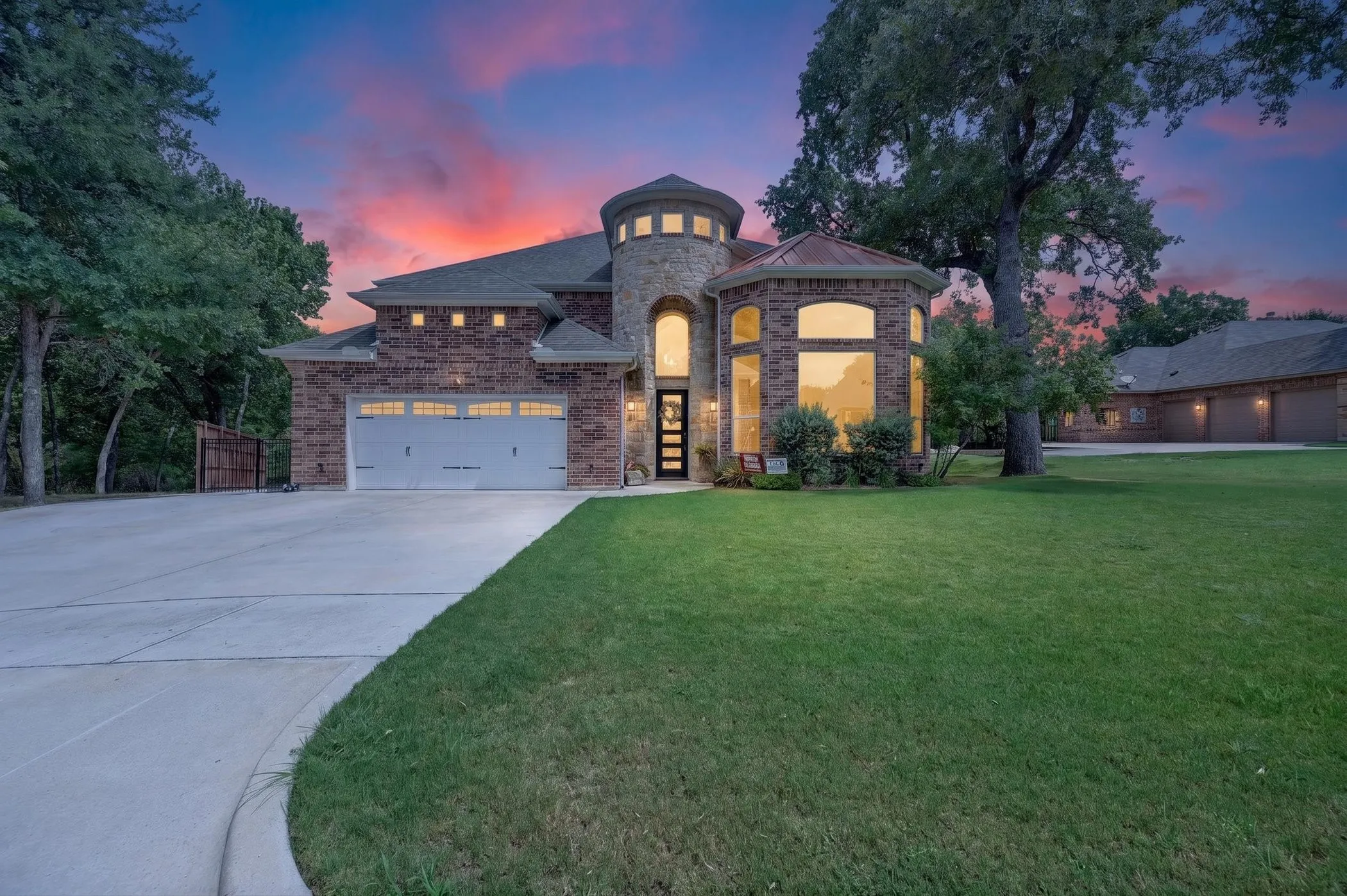 Brick exterior with a conical turret, two attached garage doors, expansive concrete driveway, and a separate garage structure
