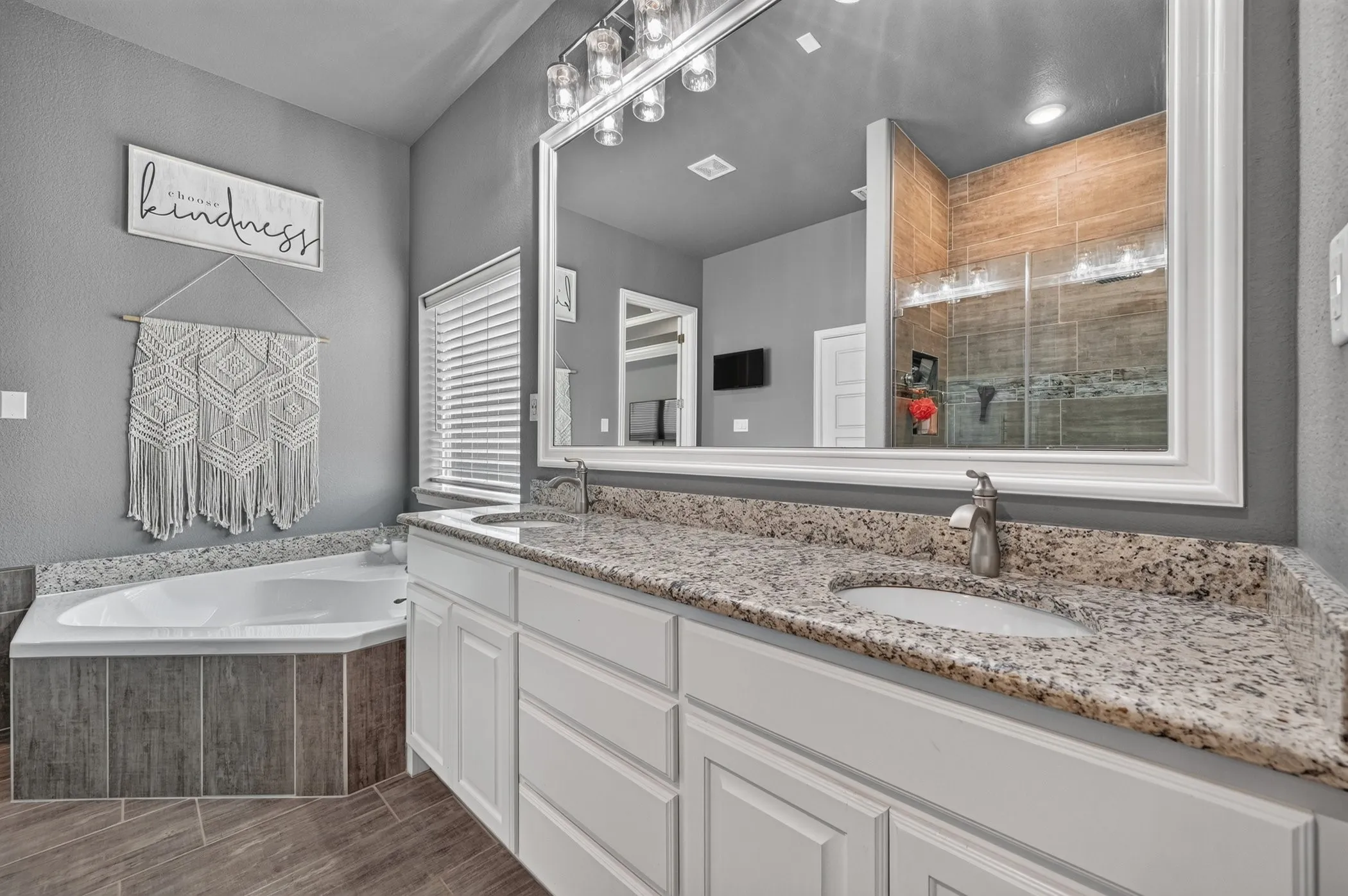 Dual vanity with a stone countertop and undermount sinks, set below a large framed mirror with integrated lighting