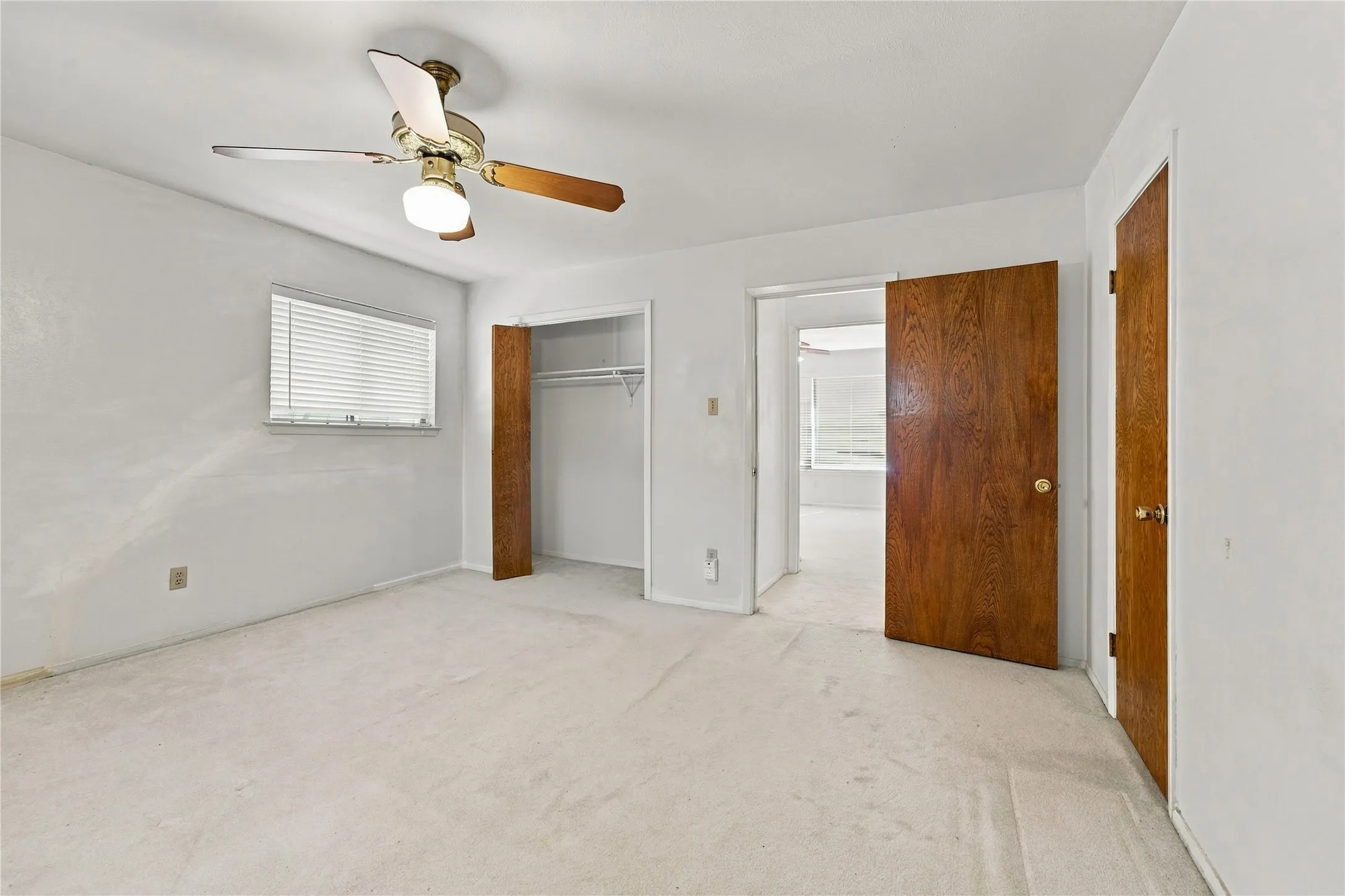 Recessed window with blinds, ceiling fan with integrated lighting, wood-paneled doors, and wall-to-wall carpeting