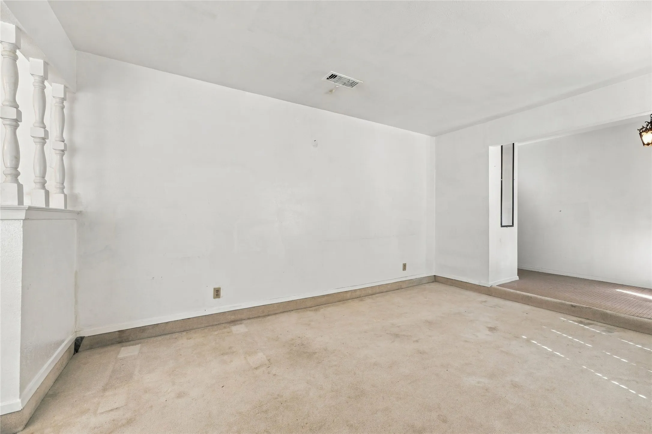 Spacious room featuring light-colored carpet, white walls, and a decorative balustrade