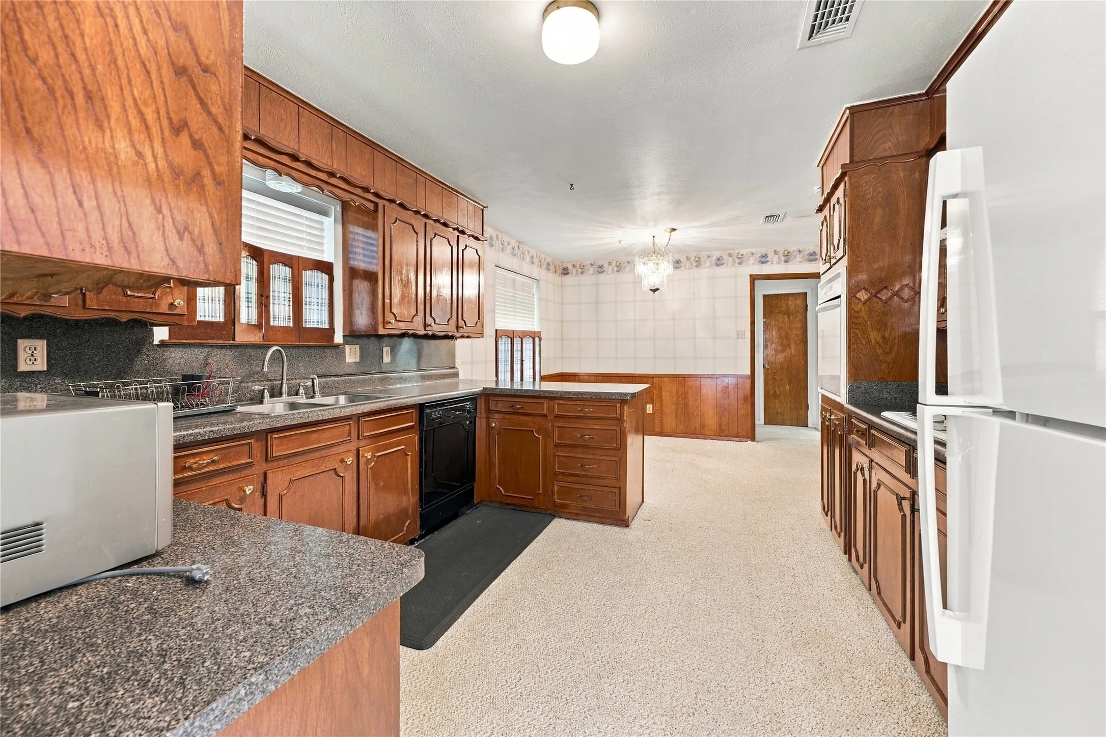 Kitchen featuring wood-finish cabinetry, granite-style countertops, a stainless steel sink, and light-colored flooring