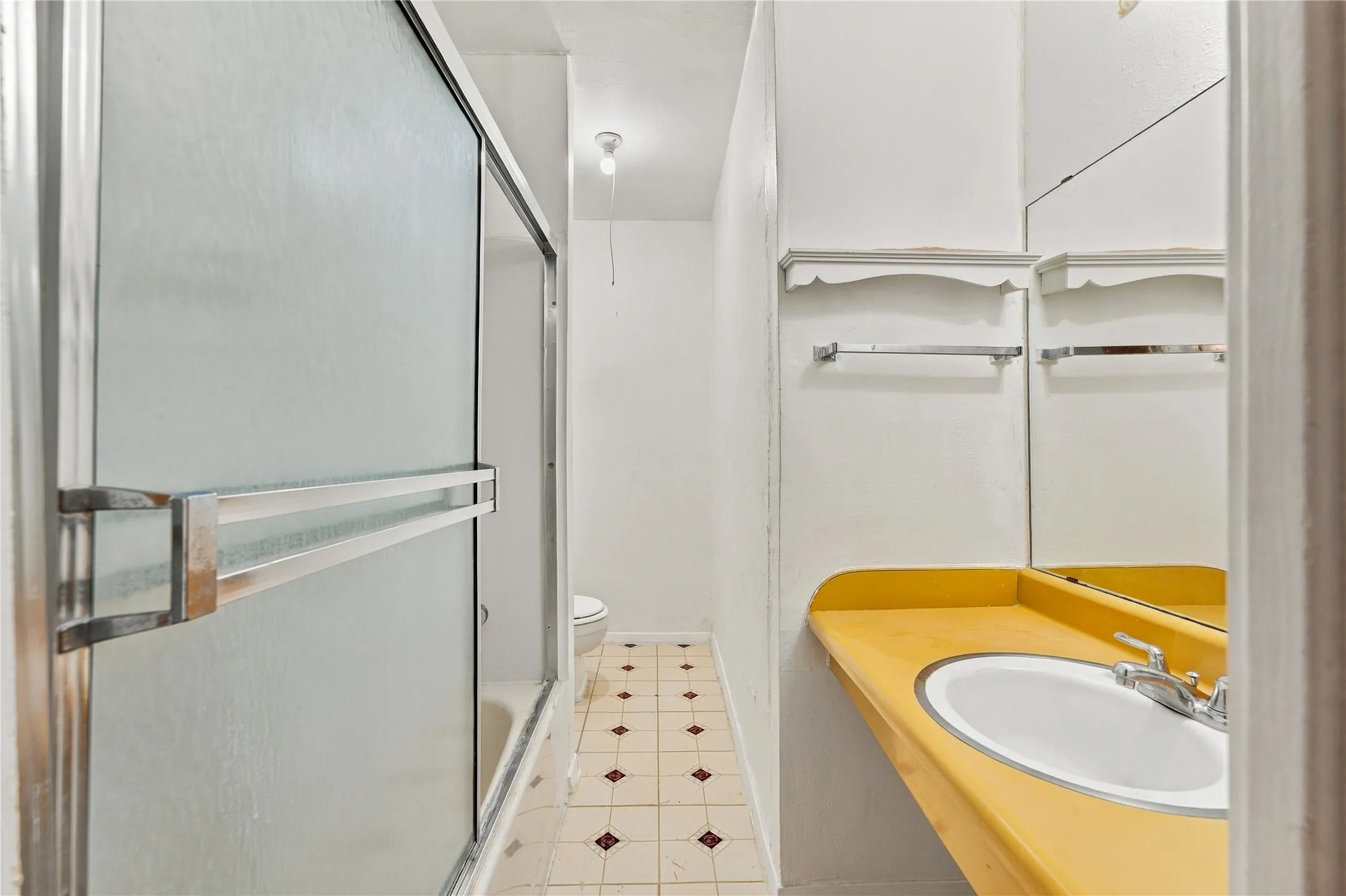 Frosted glass shower enclosure, integrated shower/tub, vanity with an integrated sink, wall-mounted mirror, and tile flooring
