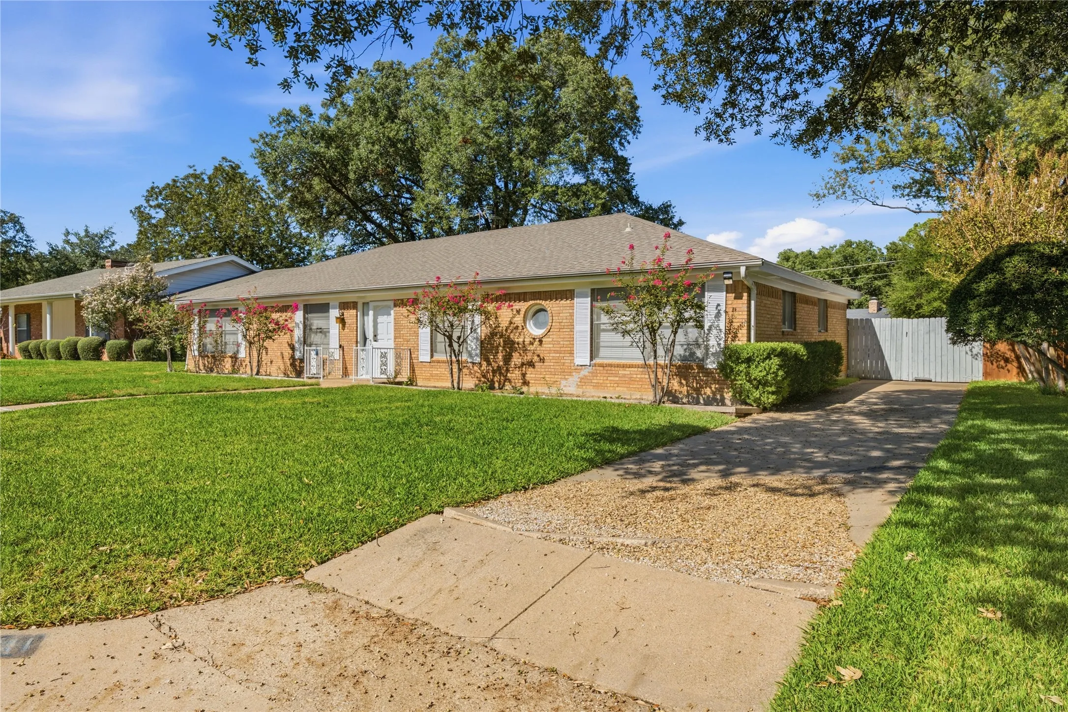 Brick exterior with a light-colored roof, a concrete driveway with gravel accents, and a white privacy fence