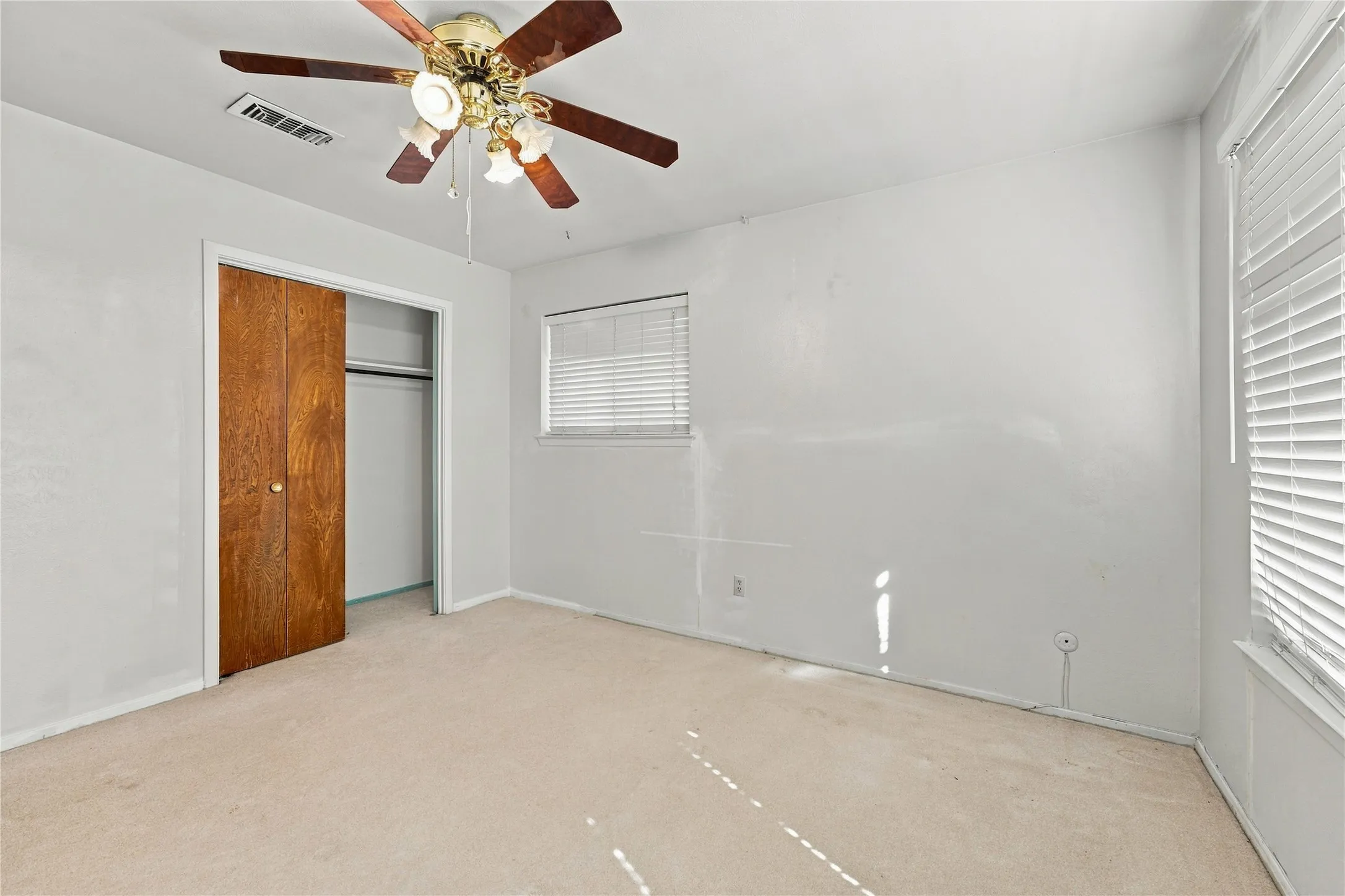 Recessed window with horizontal blinds, built-in closet with bi-fold wood doors, and ceiling fan with integrated lighting
