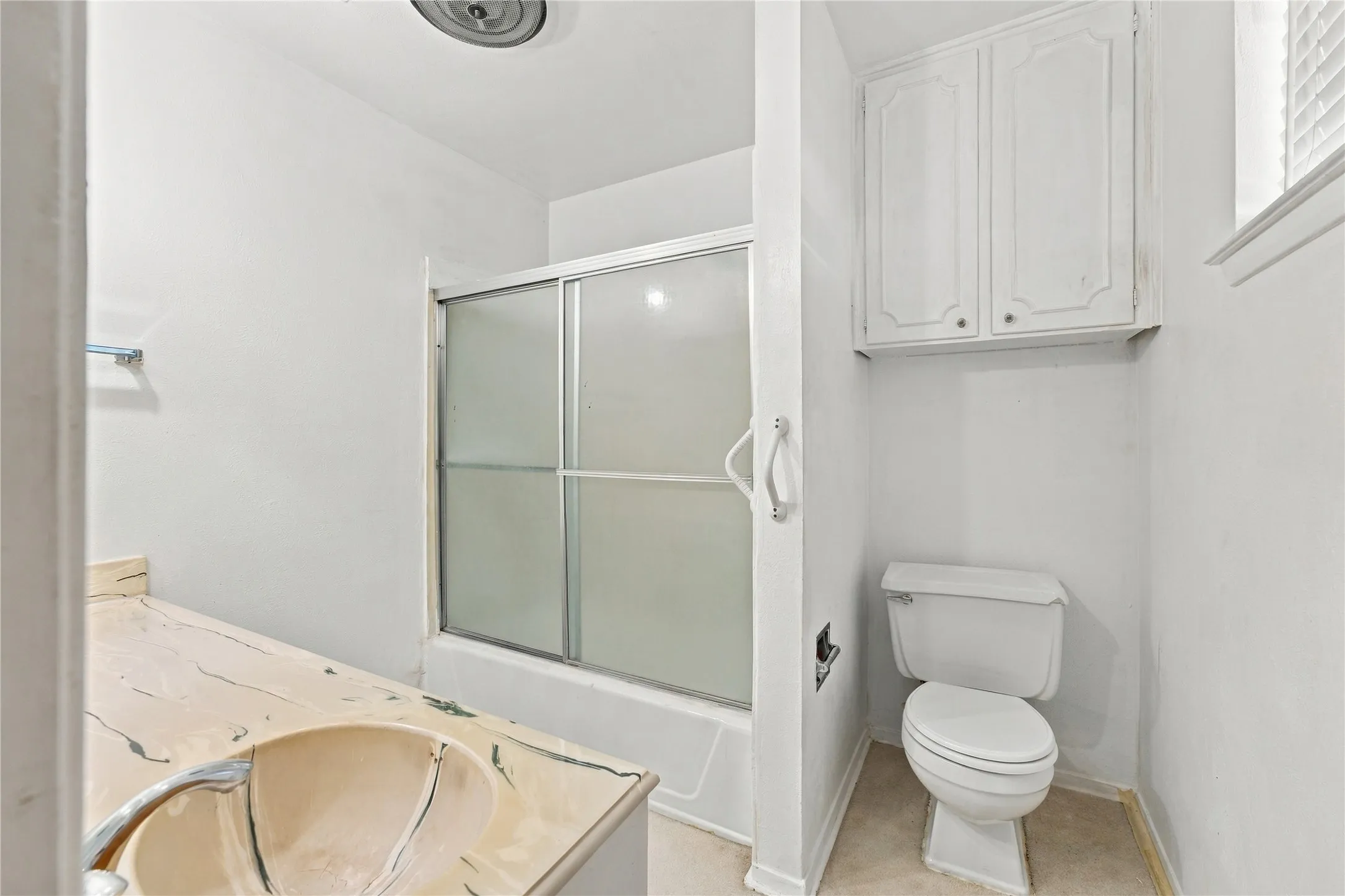 Built-in cabinetry, shower with sliding glass doors, white toilet, and countertop with integrated sink