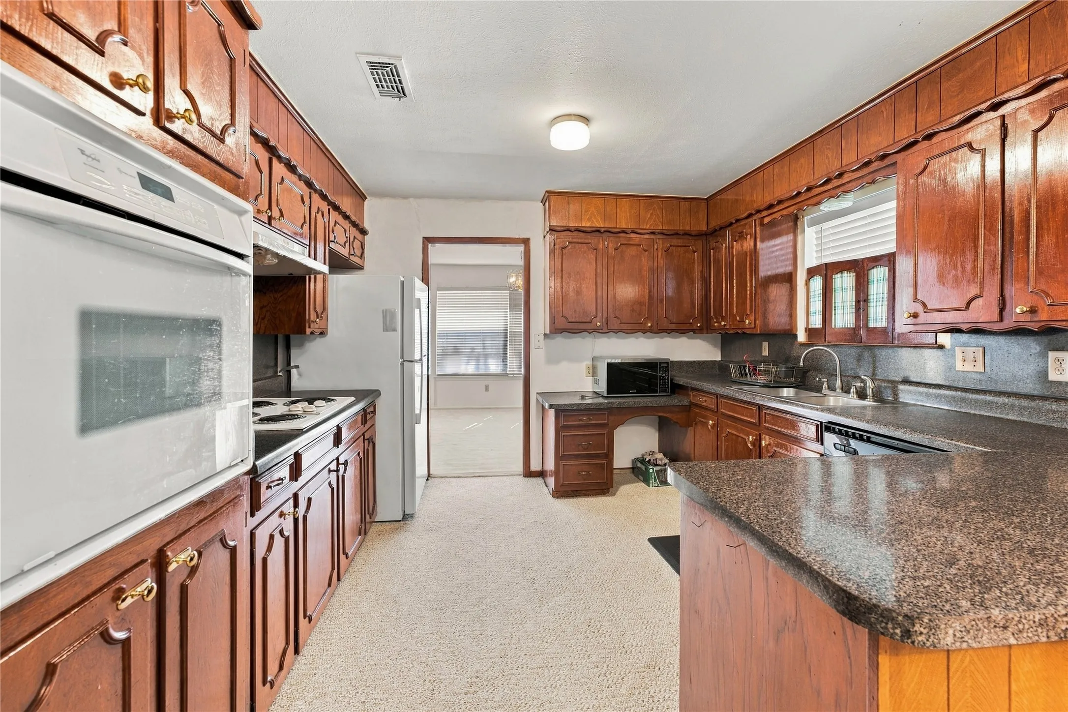 Kitchen featuring wood cabinetry, built-in oven, integrated cooktop, and speckled countertops