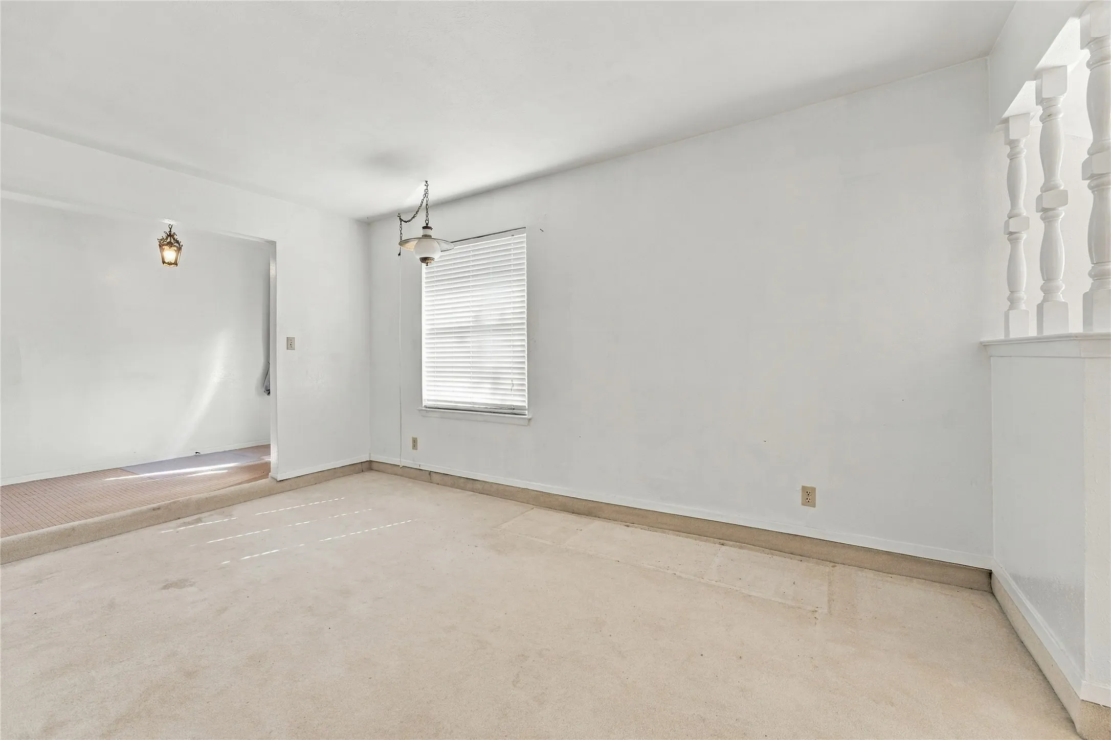 Recessed ceiling, neutral wall color, window with blinds, suspended light fixture, half-wall with balusters