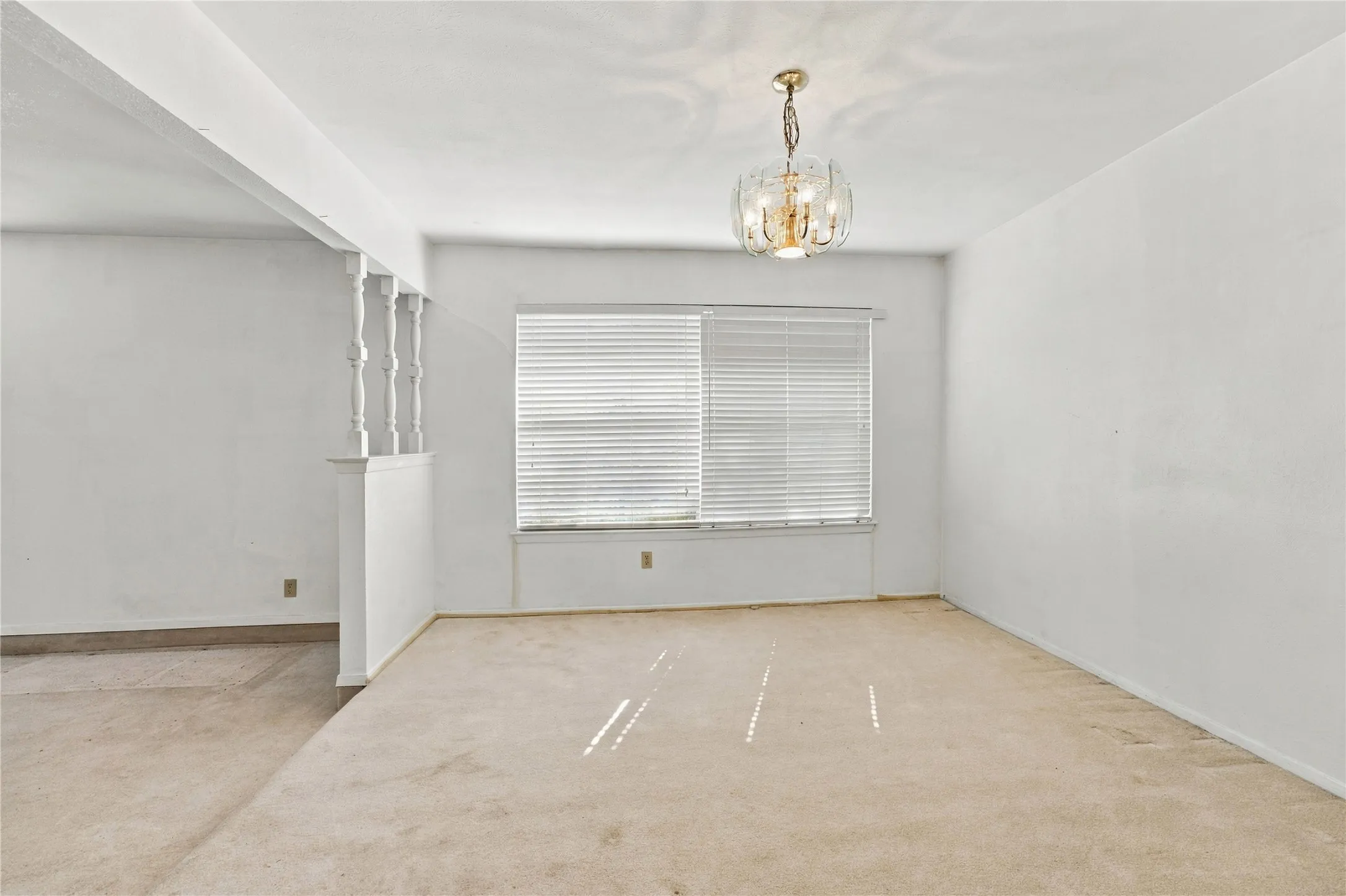Recessed window, modern chandelier, carpeted flooring, white wall finishes, and a decorative half-wall with balusters