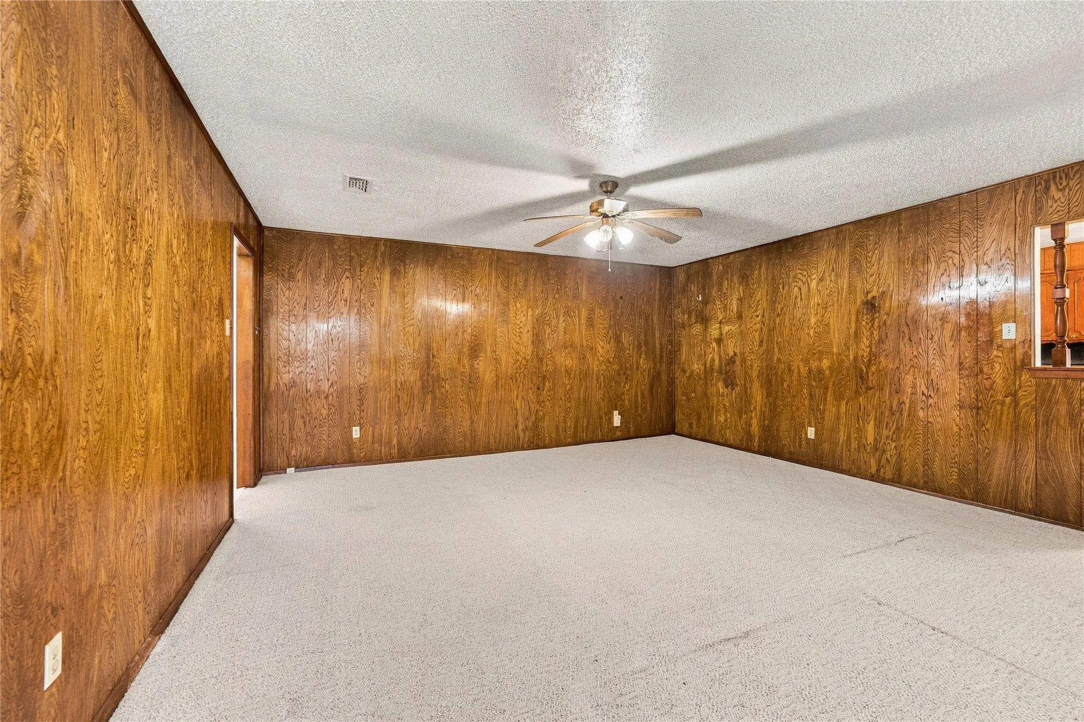 Wood-paneled walls, light-colored carpet, ceiling fan with integrated lighting, and a window opening to an interior space