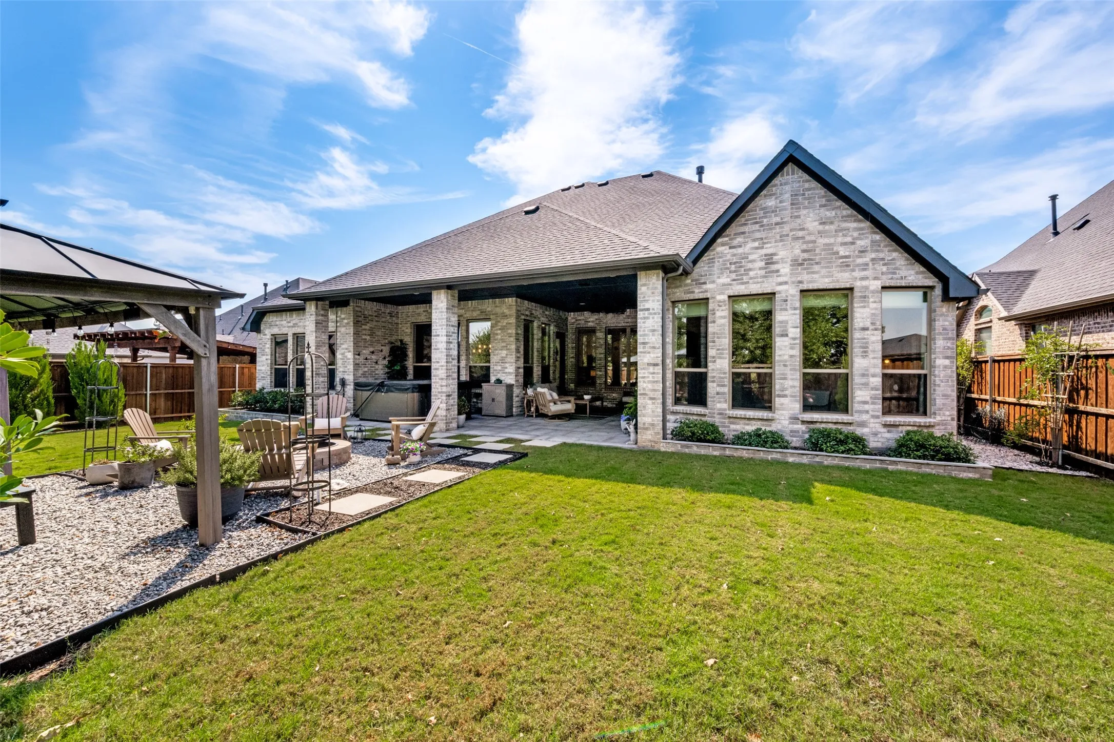 Expansive backyard featuring a manicured lawn, a gravel path with stepping stones, a covered patio, and a privacy fence