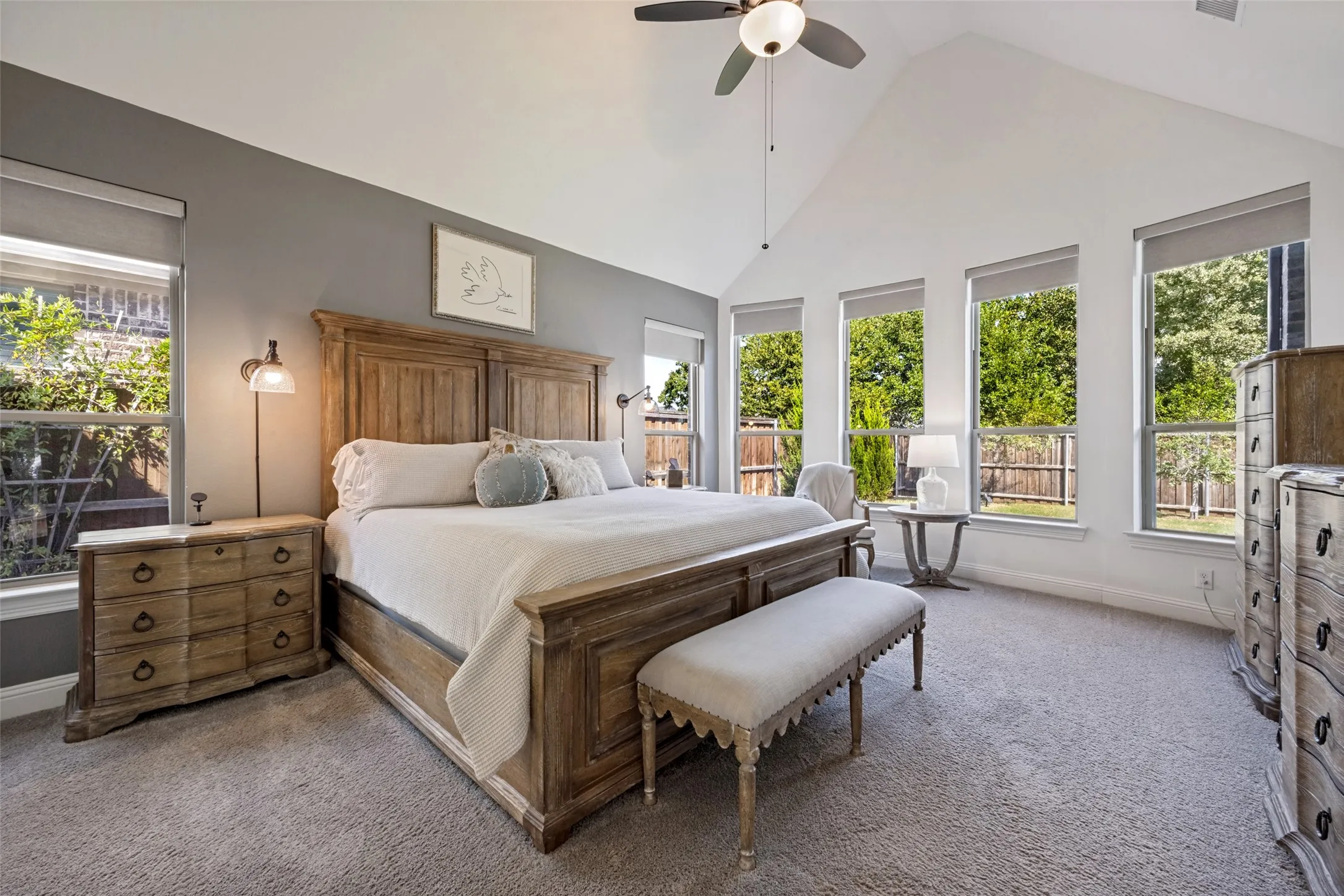Vaulted ceiling with ceiling fan, multiple windows with roller shades, and grey wall accents