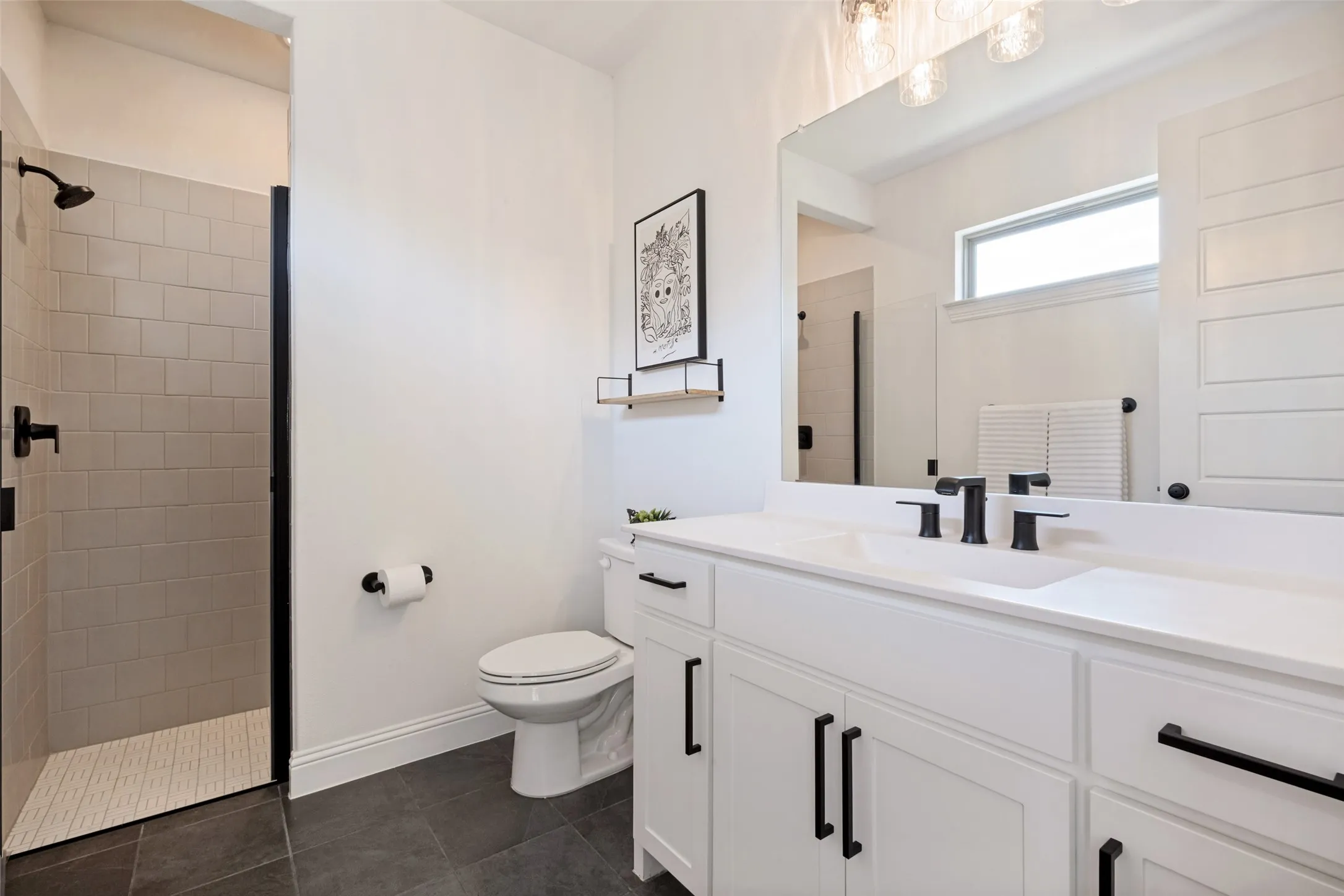 White shaker-style vanity with matte black hardware, integrated sink, and dark tiled flooring