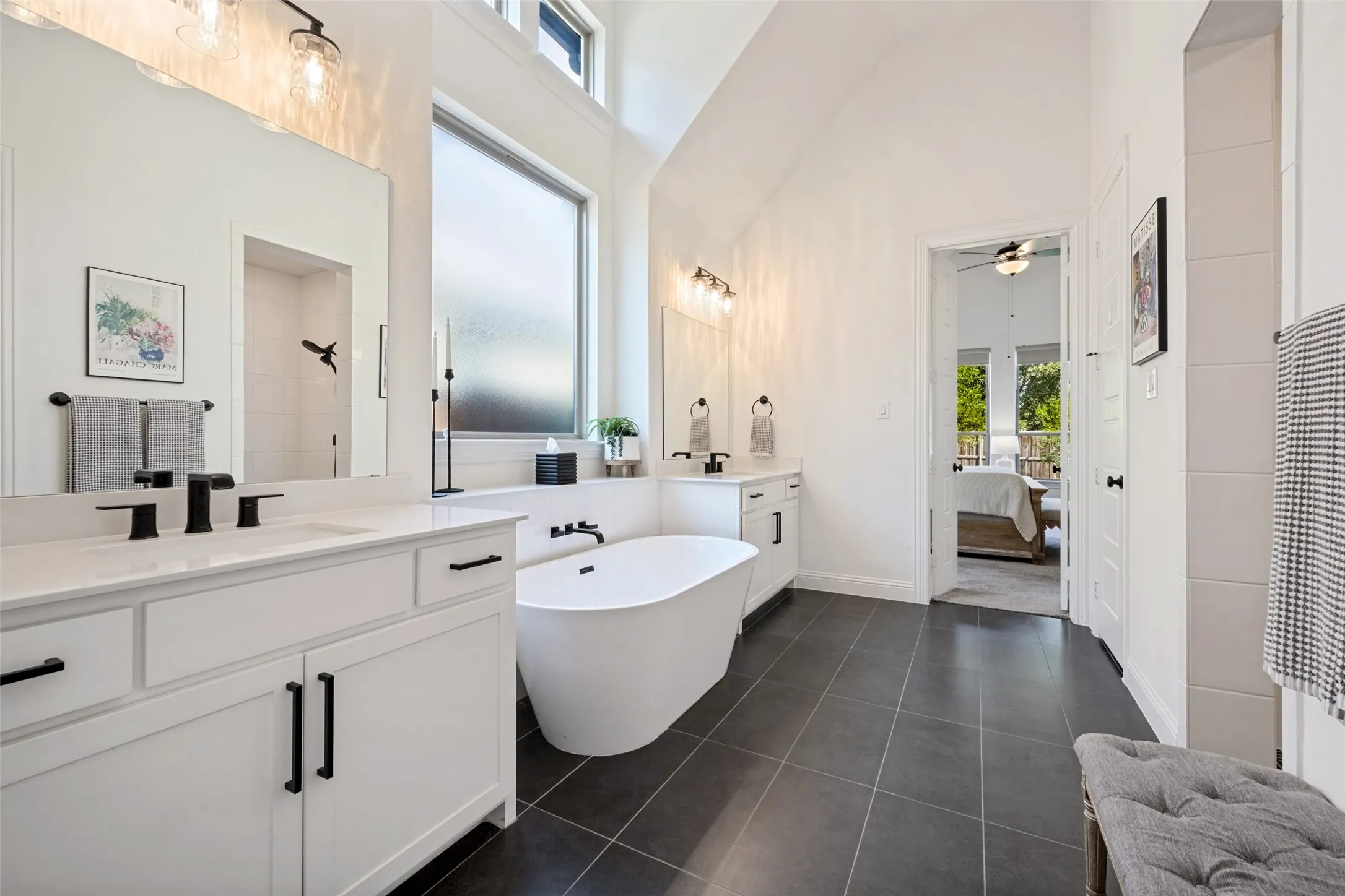 Dual vanity with white cabinetry, freestanding soaking tub, and black hardware