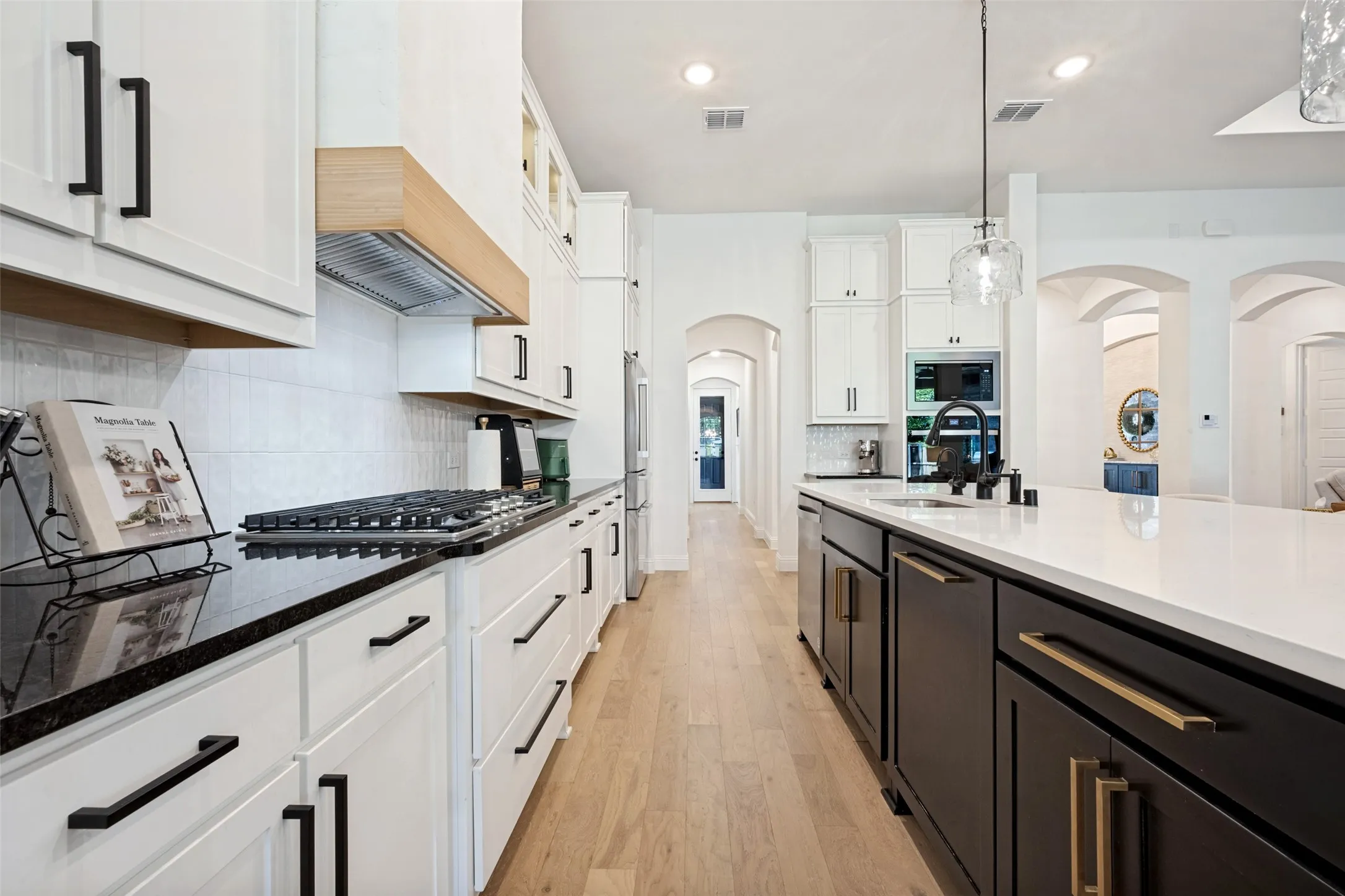 Gourmet kitchen with white cabinetry, black countertops, wood-finish flooring, a central island with white countertop, and integrated appliances