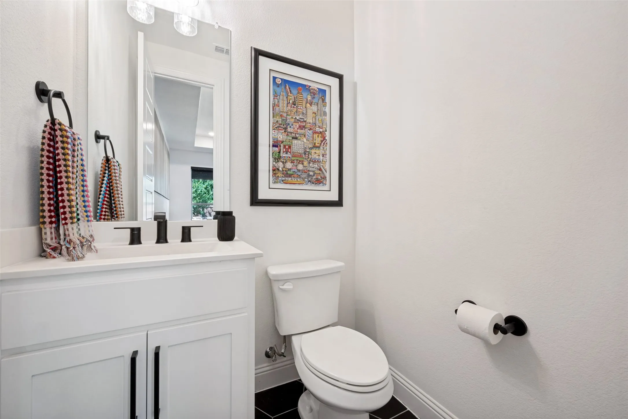 White vanity with dual cabinet storage, white countertop, matte black faucet, and black floor tiles