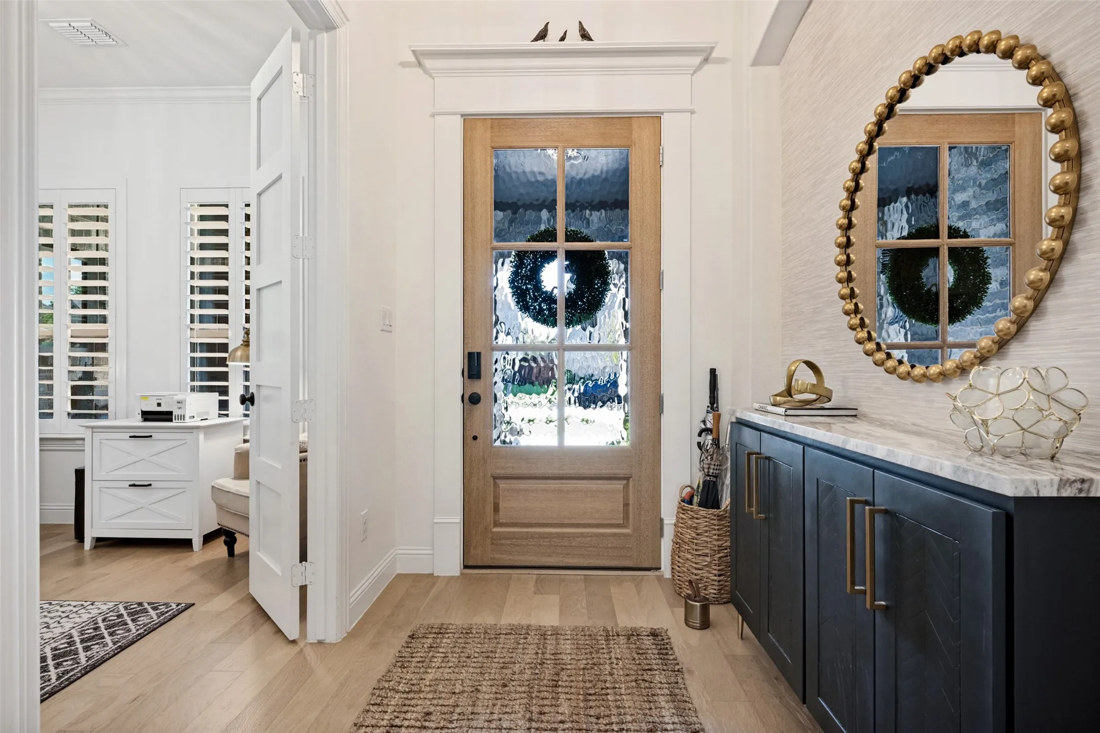 Light wood flooring, a wood front door with textured glass, and a built-in dark cabinetry unit with a stone countertop