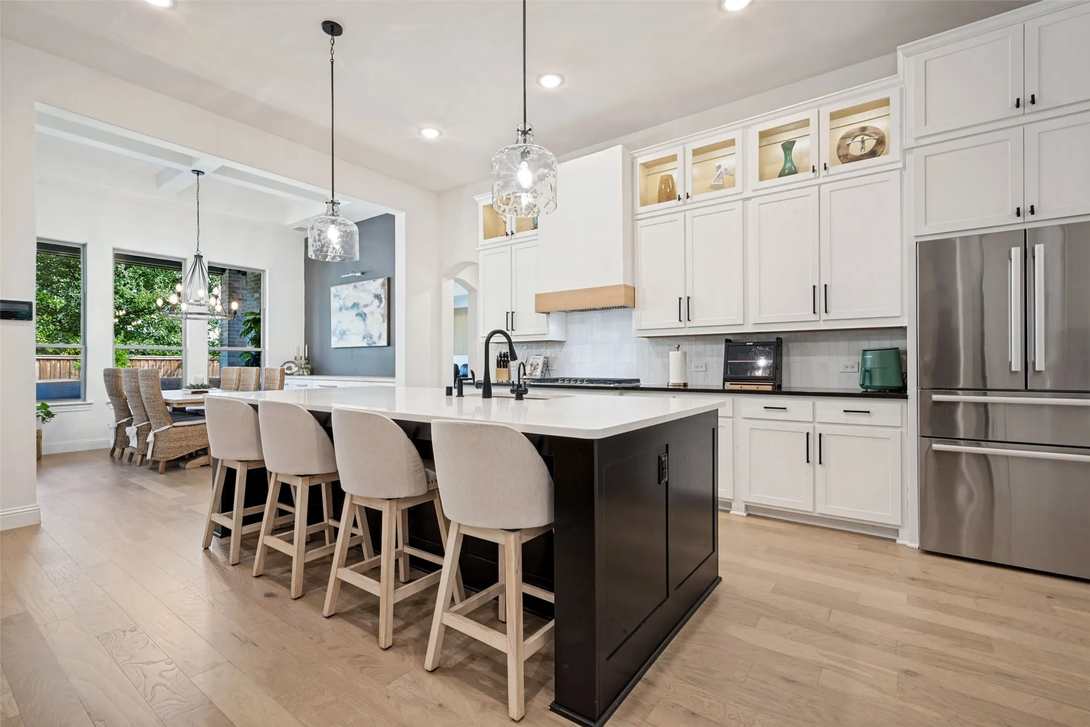 Gourmet kitchen with a large central island, light wood-finish flooring, white cabinetry with display features, stainless steel appliances, and matte black fixtures