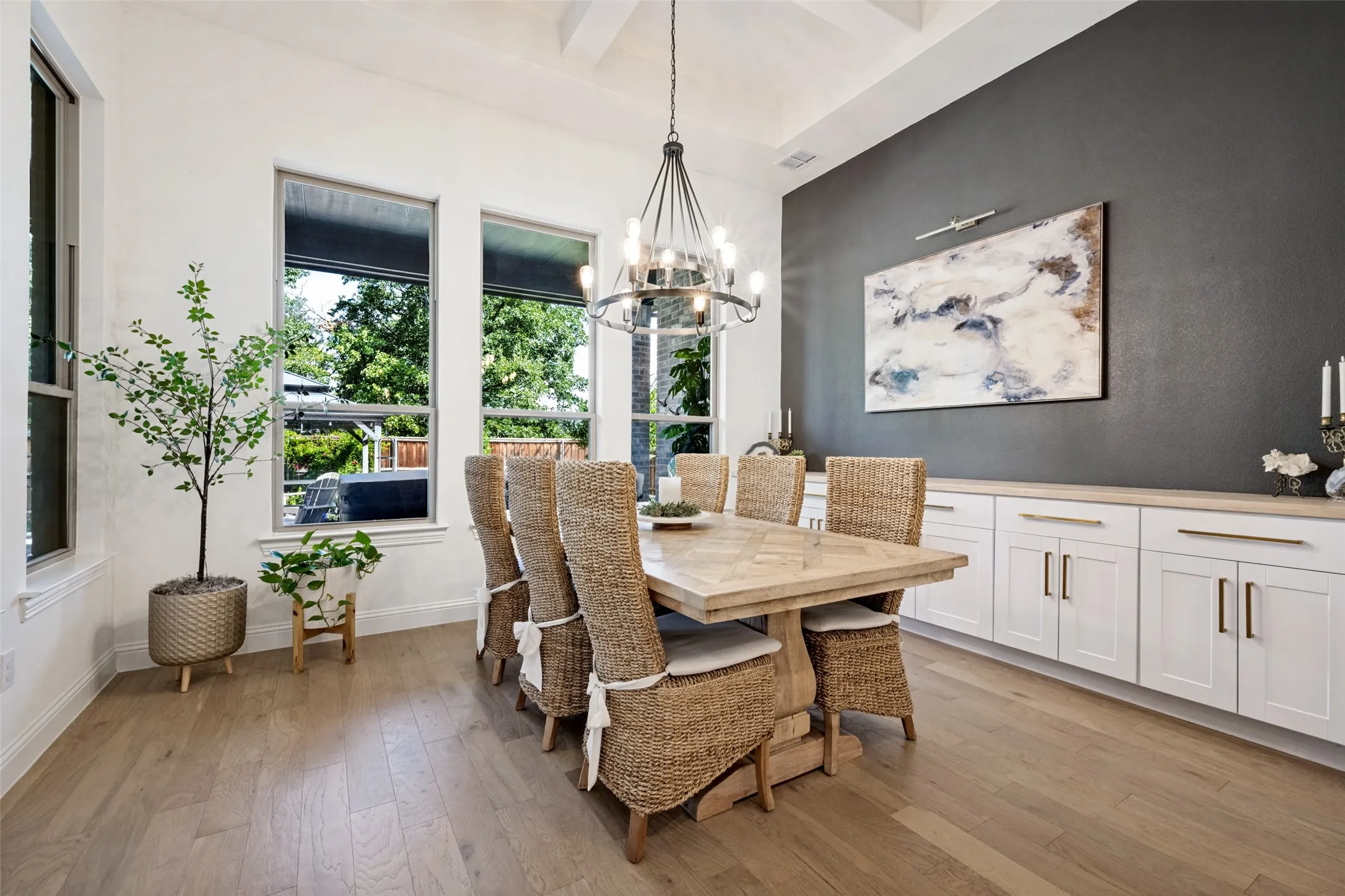 Vaulted ceiling with exposed beams, wood-finish flooring, multiple windows, built-in cabinetry with a light-tone countertop, and a chandelier lighting fixture