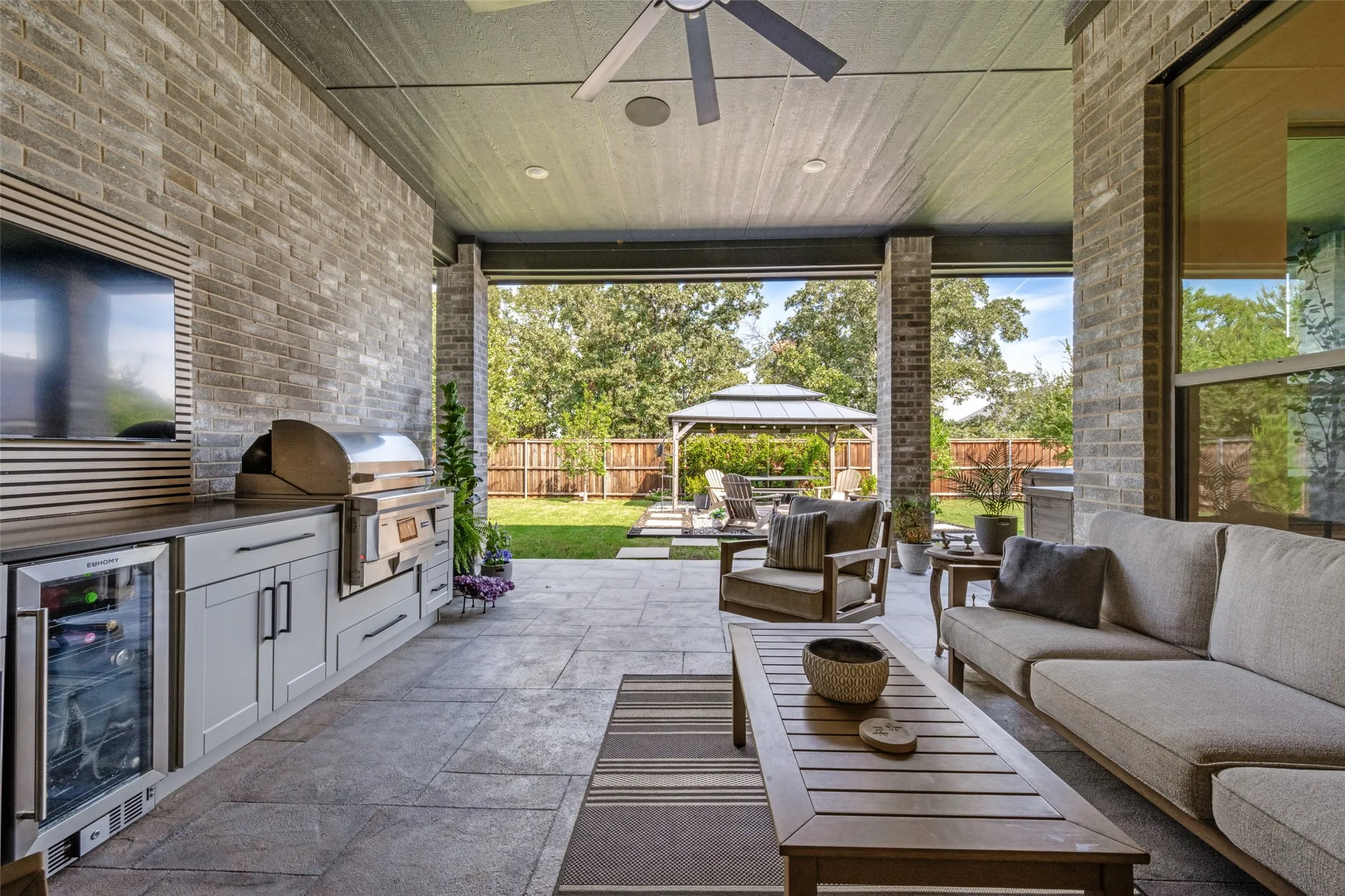 Covered outdoor living space featuring an integrated outdoor kitchen with built-in grill and beverage refrigerator