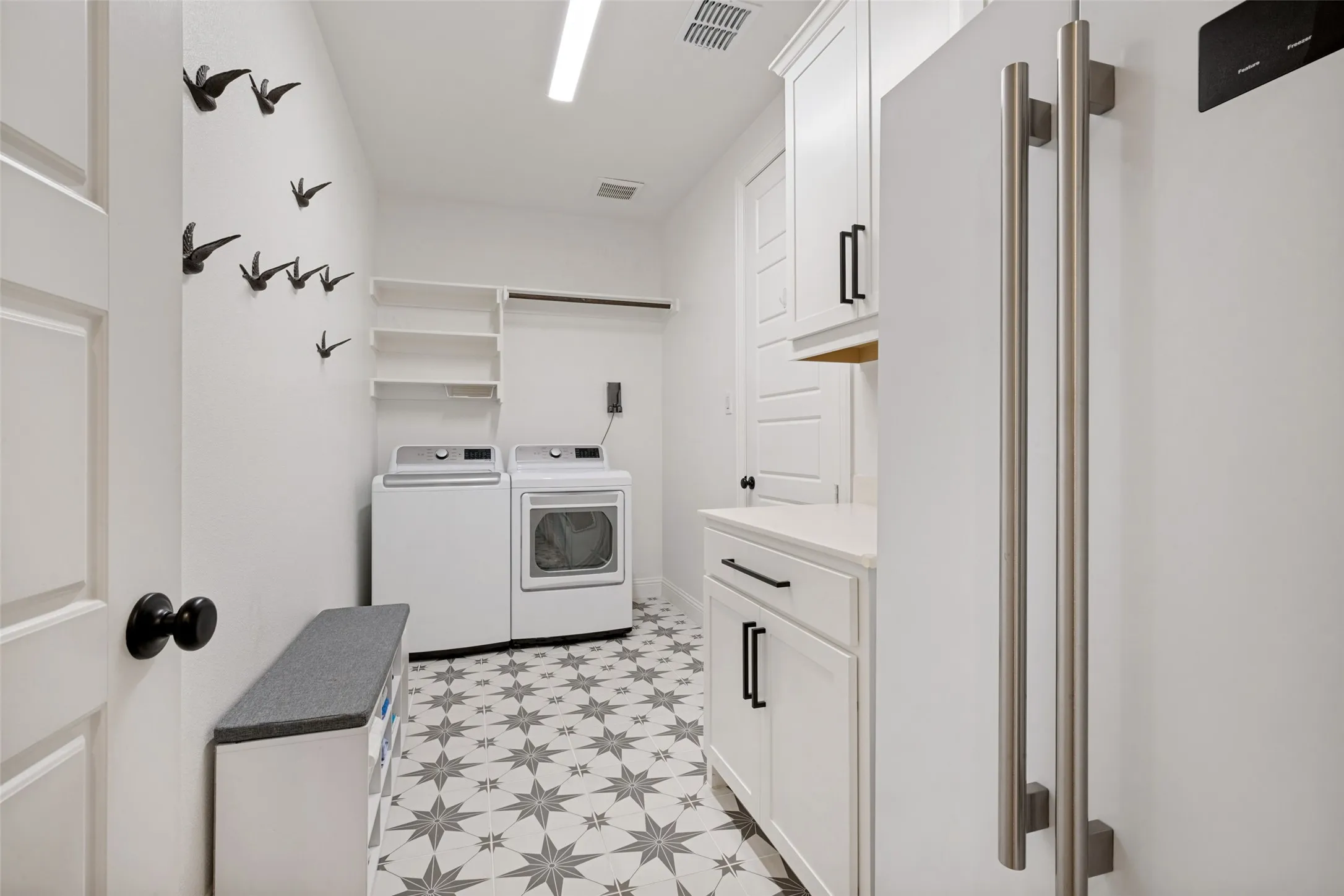 White cabinetry with matte black hardware, geometric pattern floor tile, built-in shelving, and a bright overhead light fixture