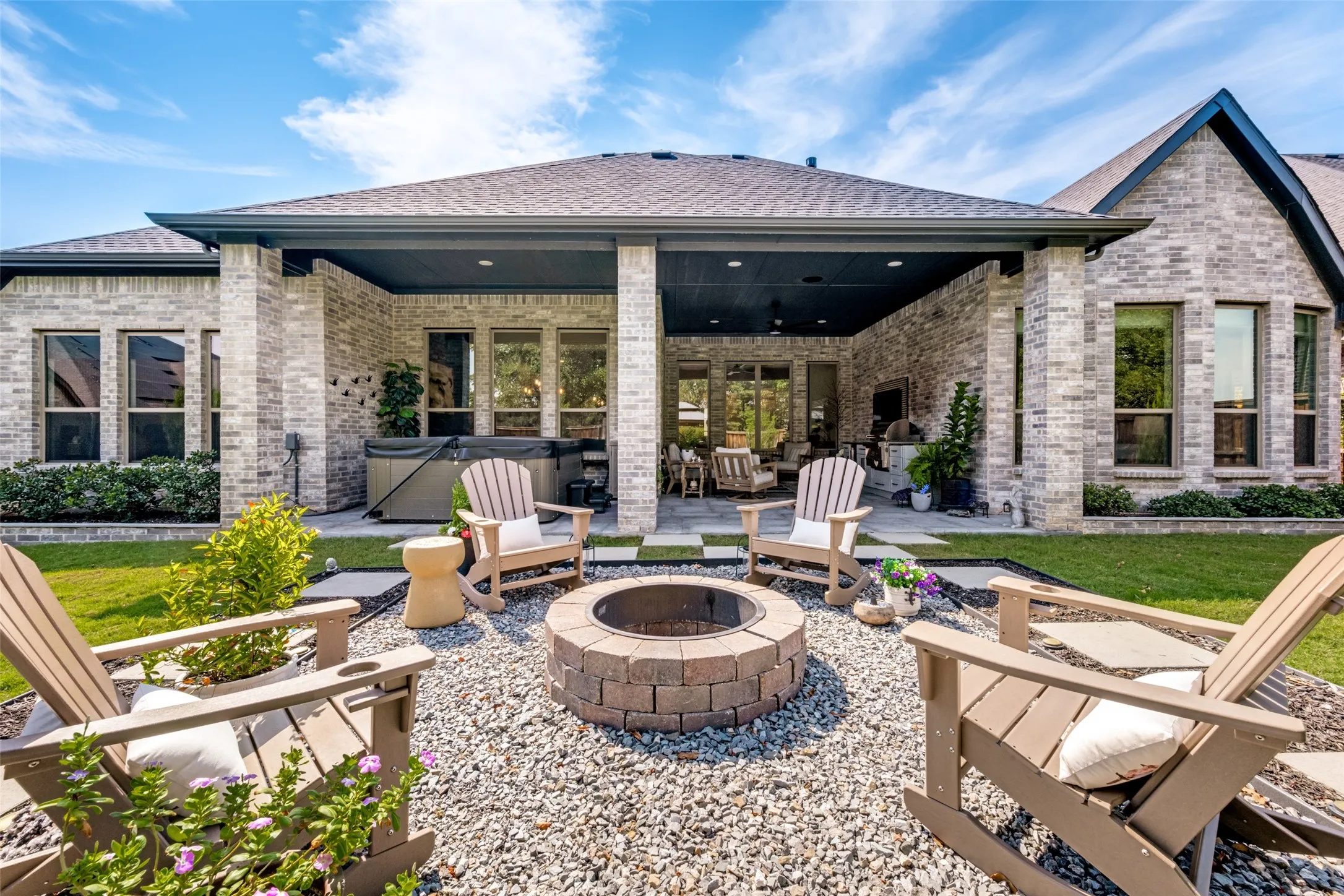 Expansive backyard featuring a stone fire pit, covered patio, hot tub, and brick exterior