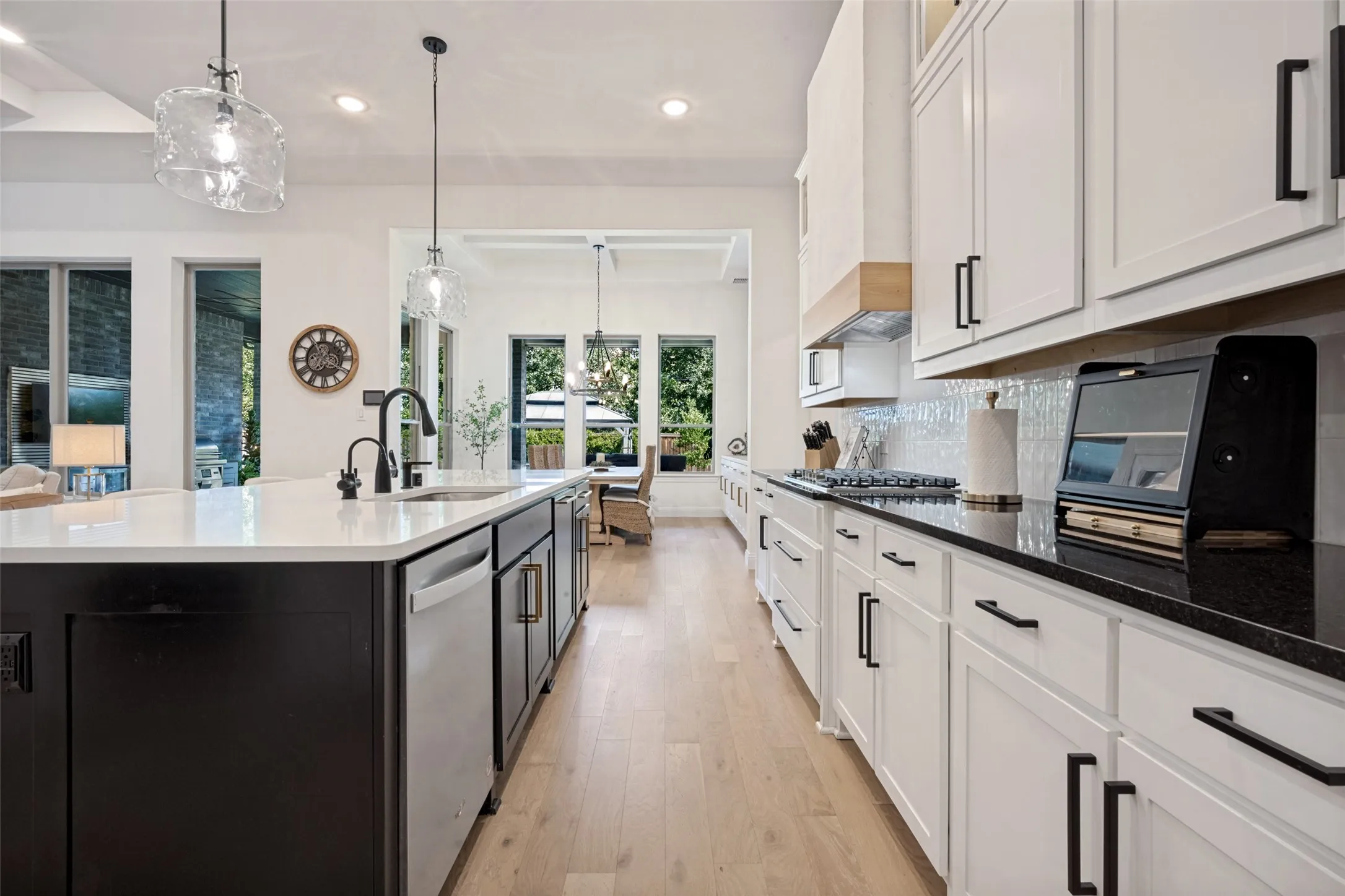 Gourmet kitchen featuring a large island with sink, white shaker cabinetry, black stone countertops, stainless steel appliances, and wood-finish flooring