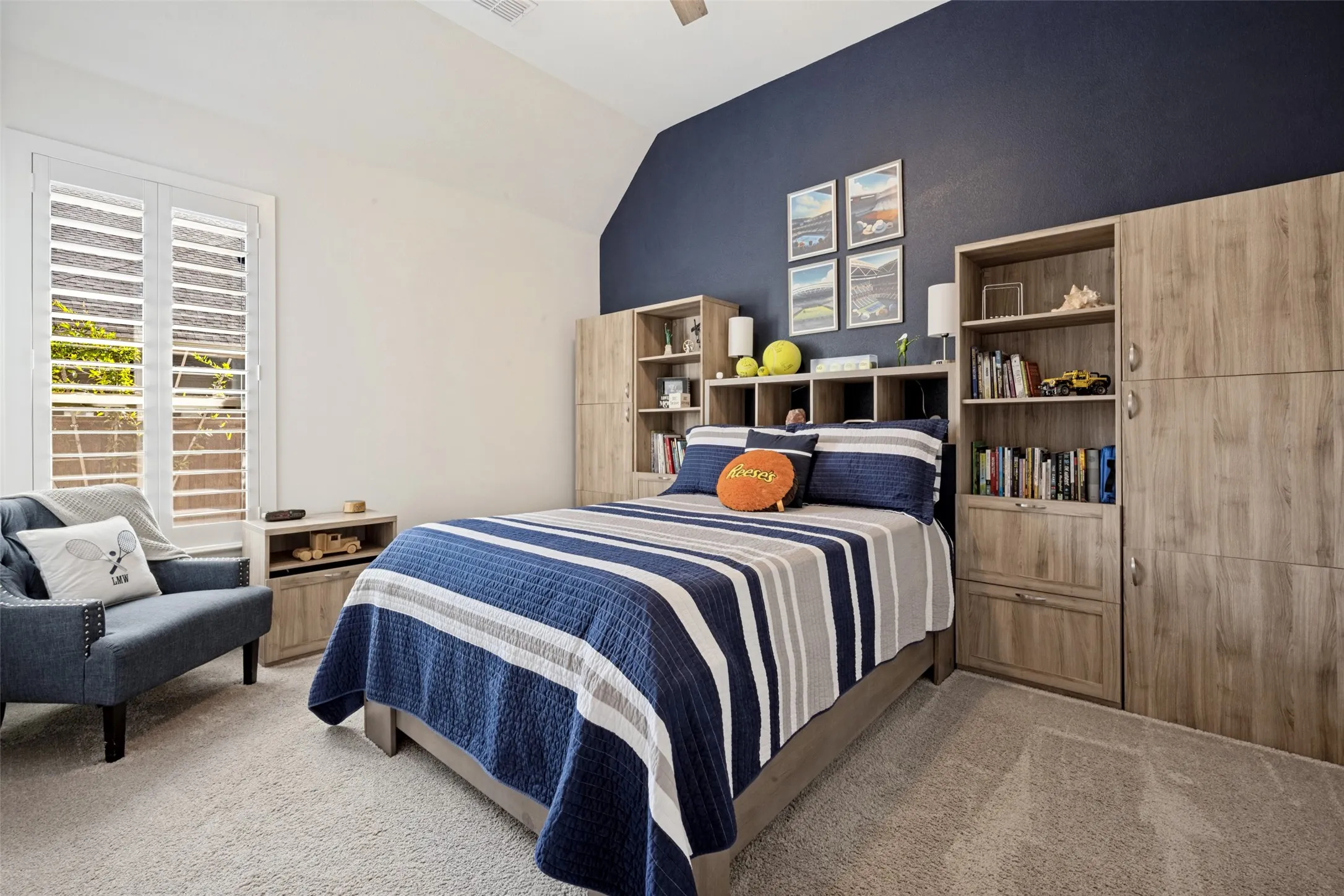 Vaulted ceiling, plantation shutters, built-in shelving, wood-finish cabinetry, and neutral carpet