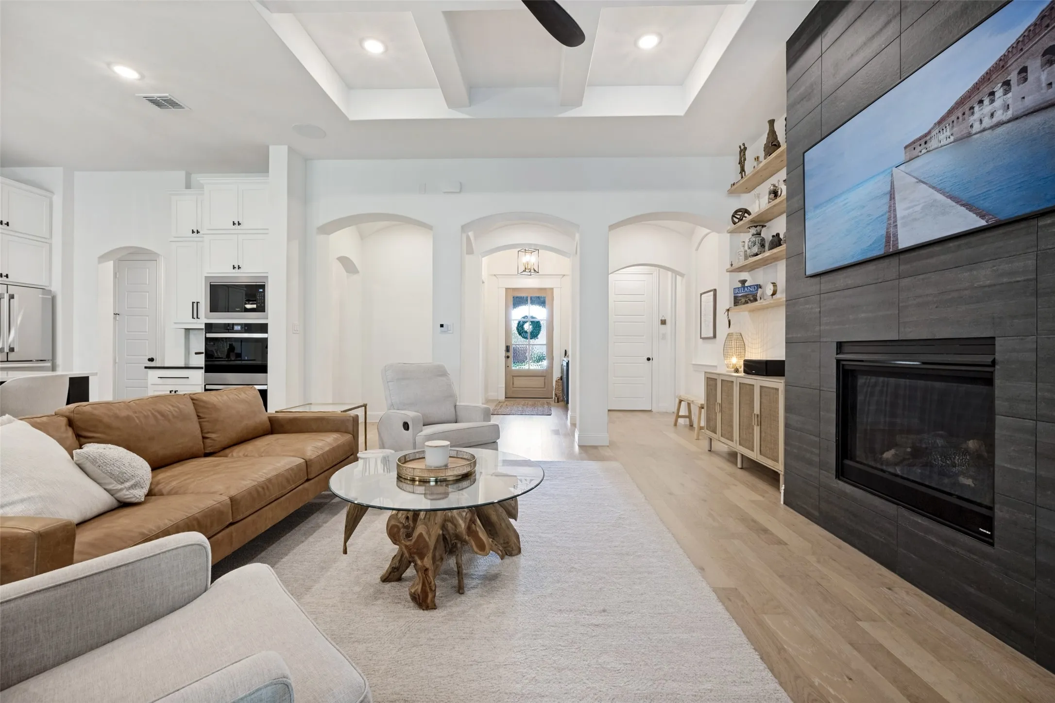 Recessed lighting, tray ceiling, dark tile fireplace surround, light wood-finish flooring, and arched doorways