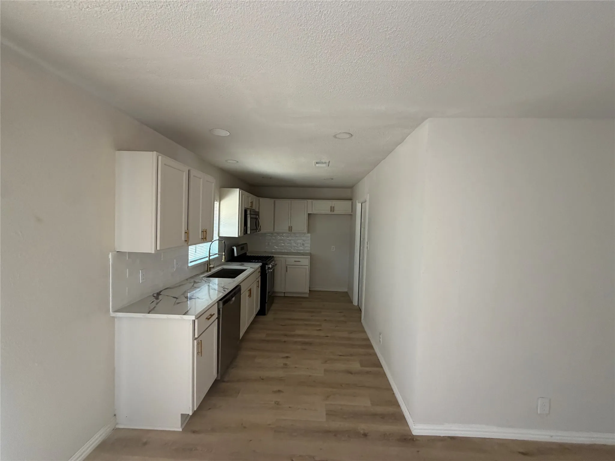 White cabinetry with gold-tone hardware, stainless steel appliances, patterned tile backsplash, wood-finish flooring, and recessed lighting