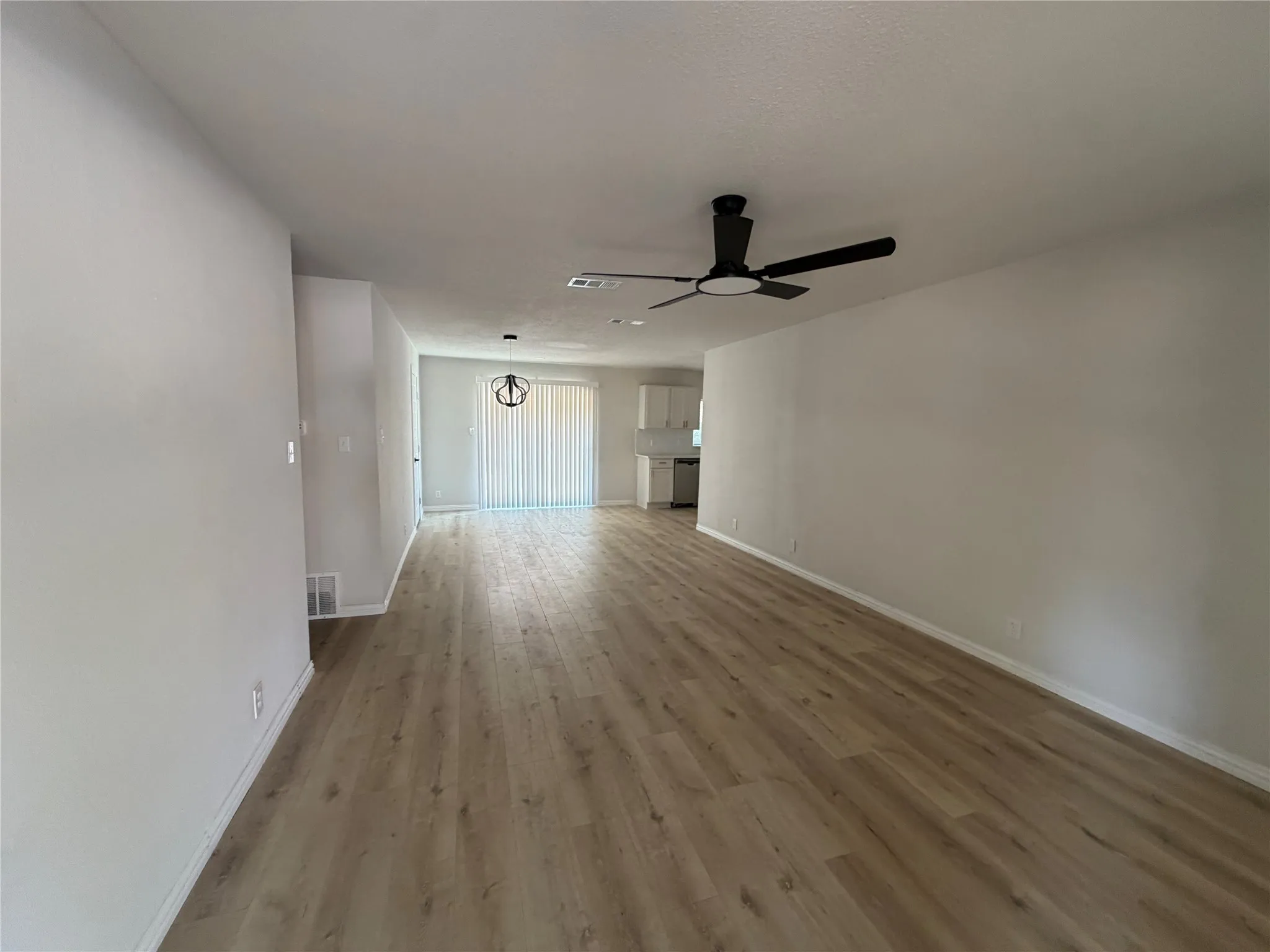Spacious living area featuring wood-finish flooring, a modern black ceiling fan, and white painted walls