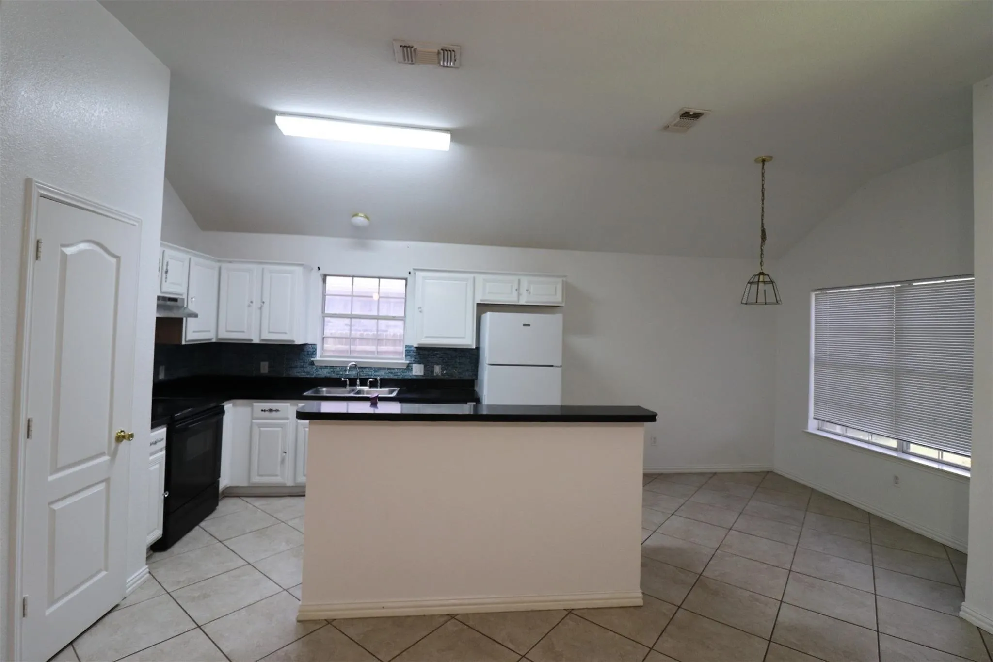 Kitchen featuring white cabinetry, black countertops, tile flooring, and a breakfast bar