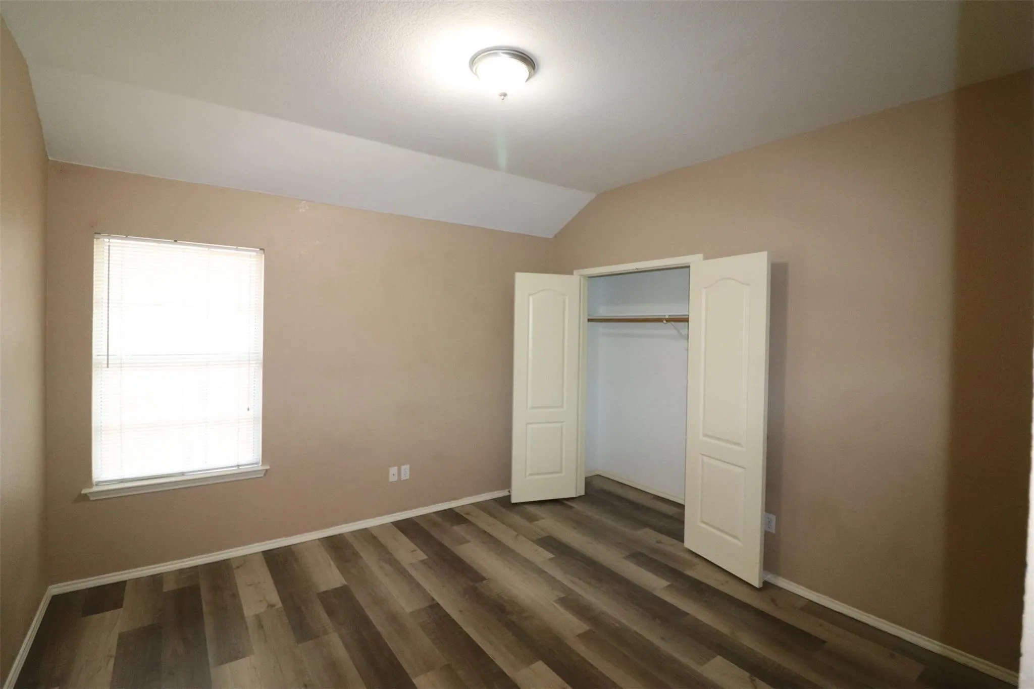 Wood-finish flooring with neutral wall tones and a vaulted ceiling