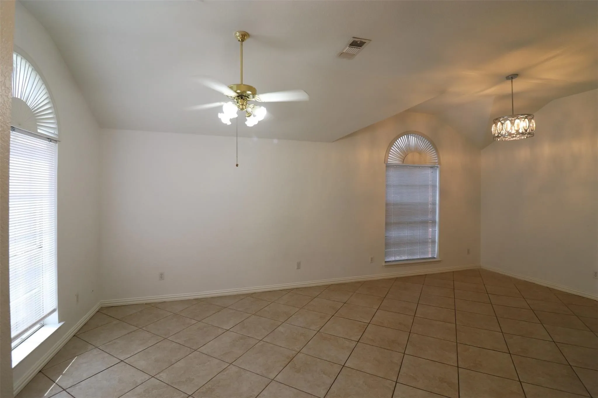Vaulted ceiling, arched windows, tile flooring, ceiling fan, and a decorative pendant light fixture