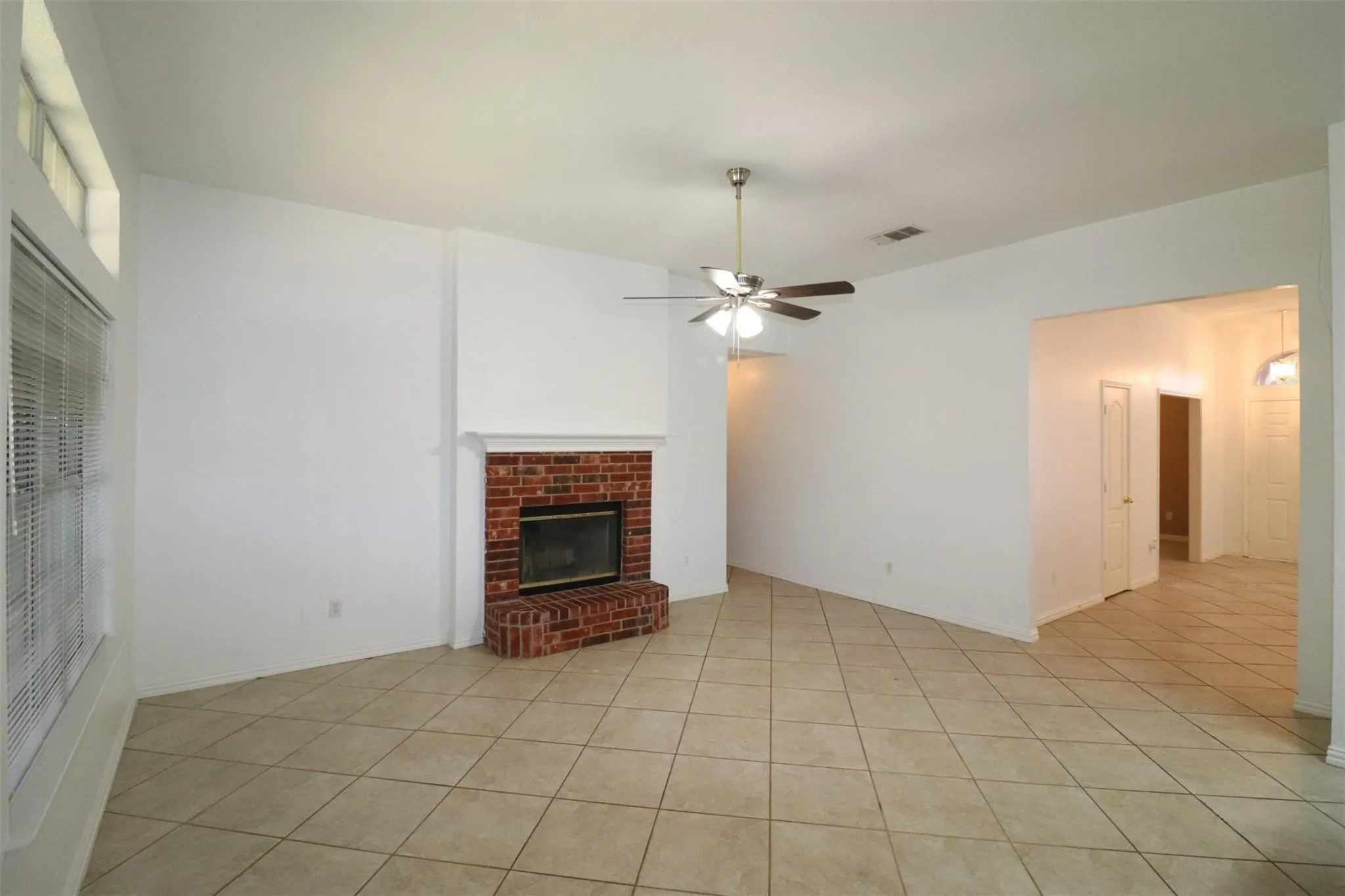 Brick fireplace with a white mantel, tile flooring, vaulted ceiling, and a ceiling fan with integrated lighting