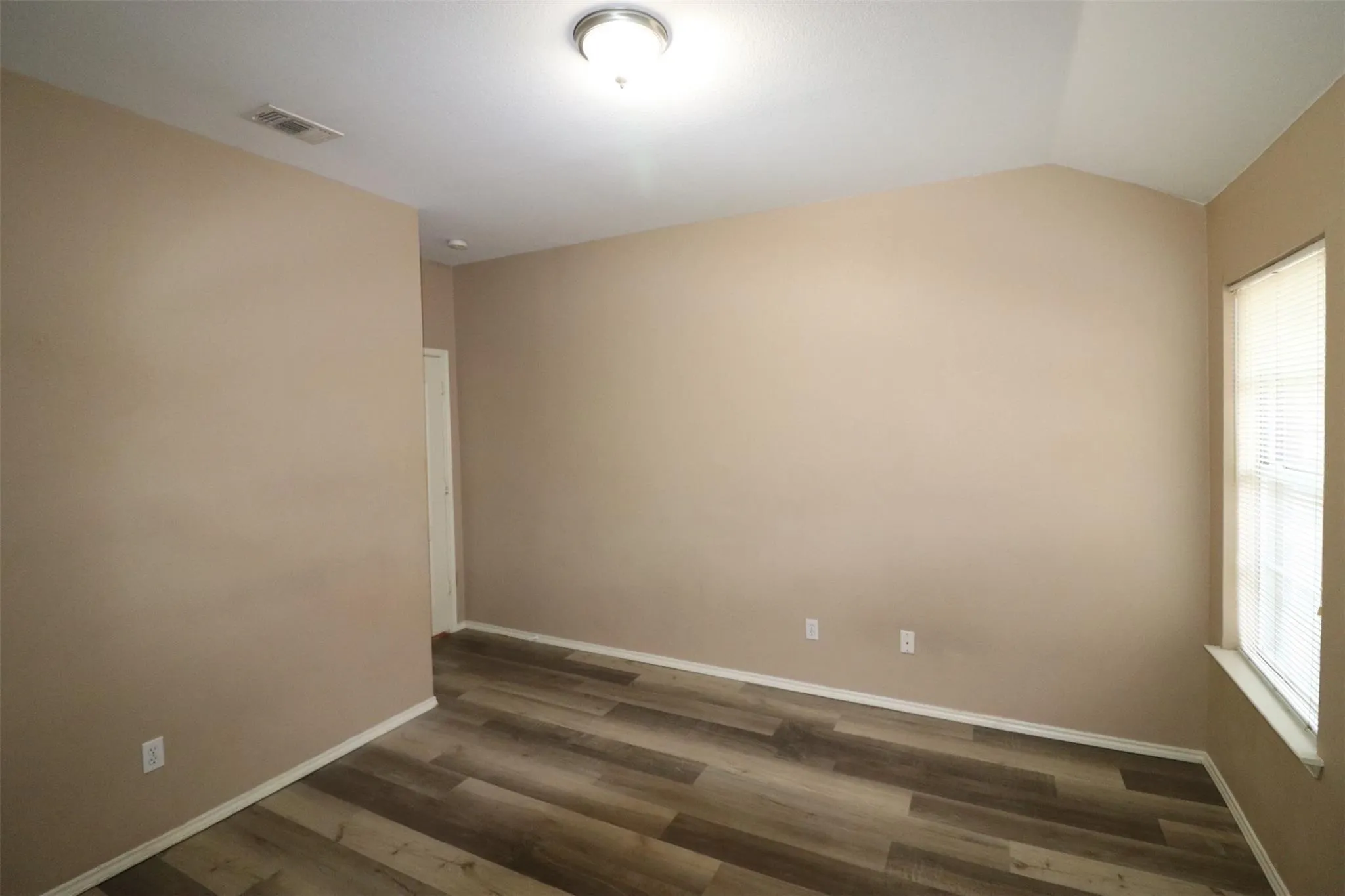 Wood-finish flooring with neutral wall tones and a vaulted ceiling