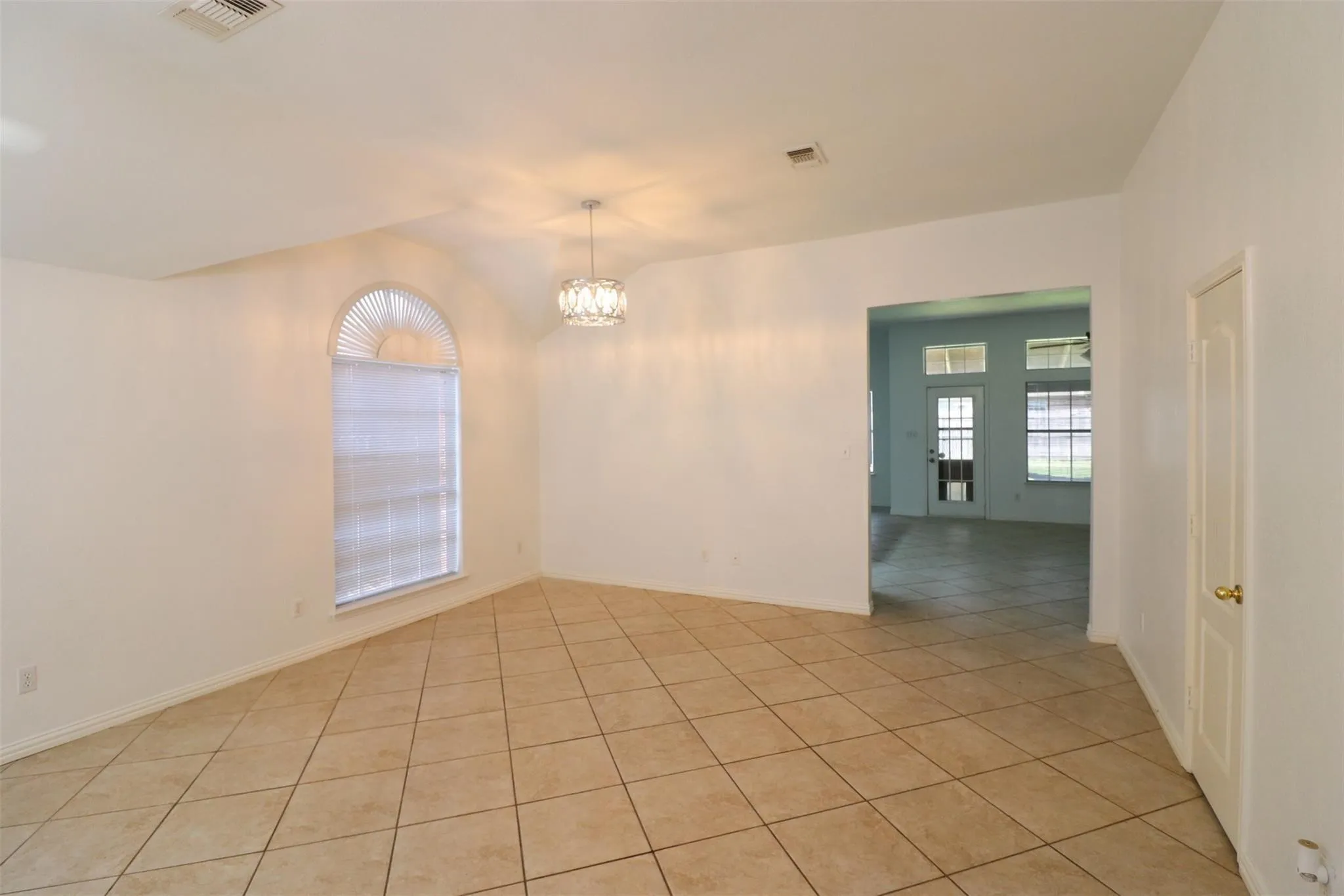 Vaulted ceiling with a contemporary chandelier, arched window with horizontal blinds, large format tile flooring, and an open doorway