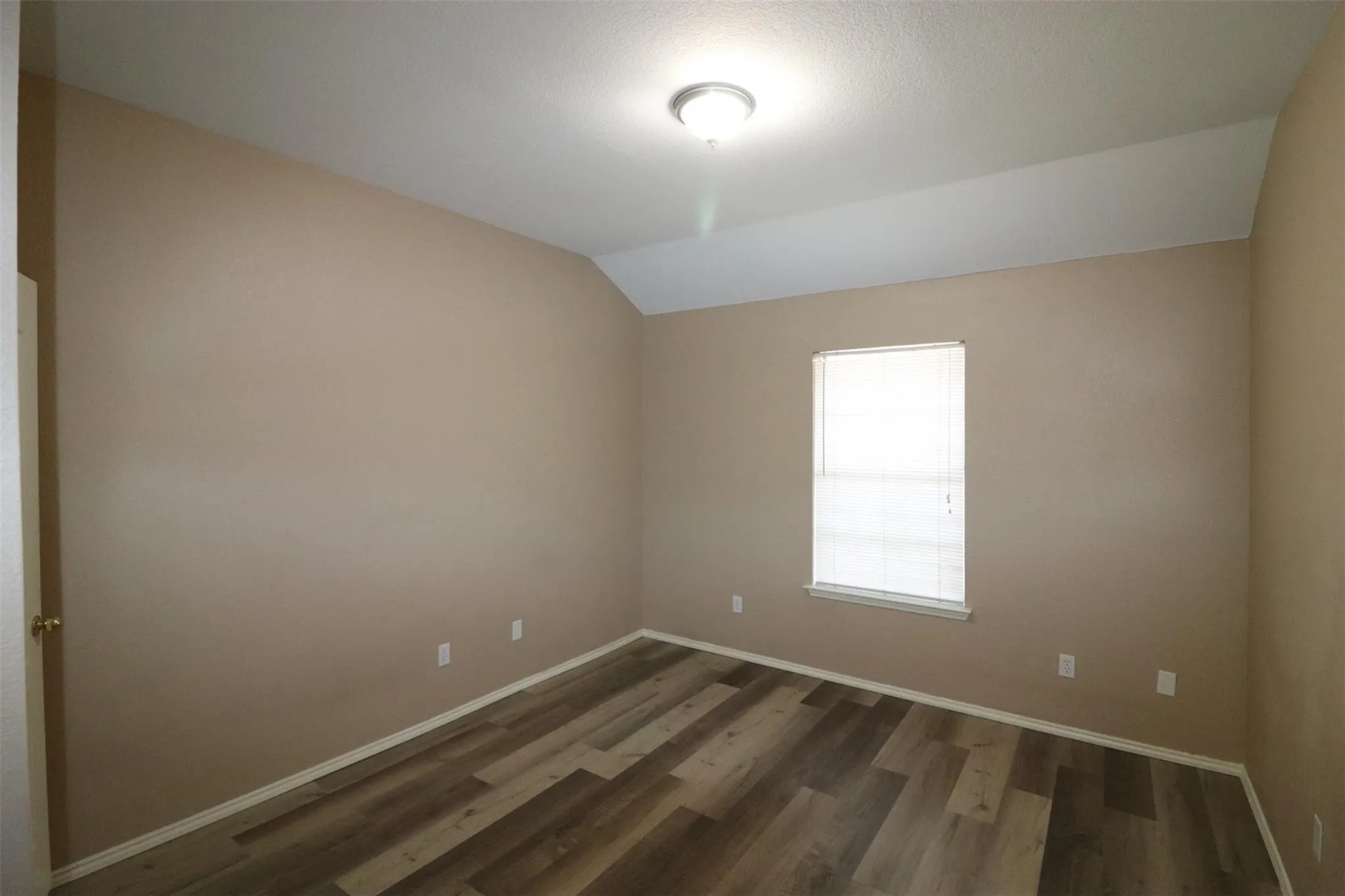 Wood-finish flooring, single window with blinds, overhead flush mount lighting, neutral wall paint, and sloped ceiling